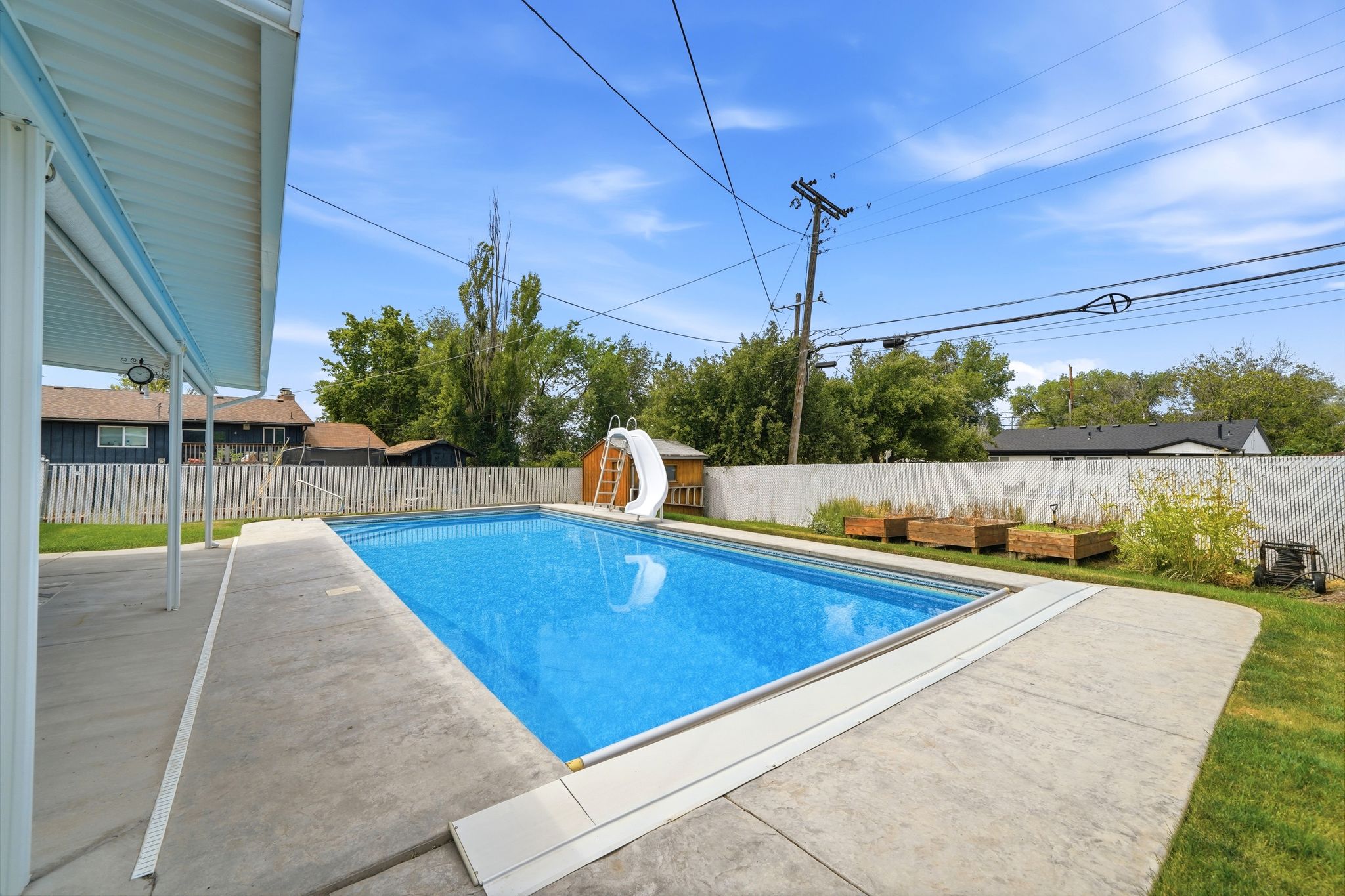 Expansive backyard featuring a rectangular in-ground swimming pool with a white slide, surrounded by stamped concrete patio areas