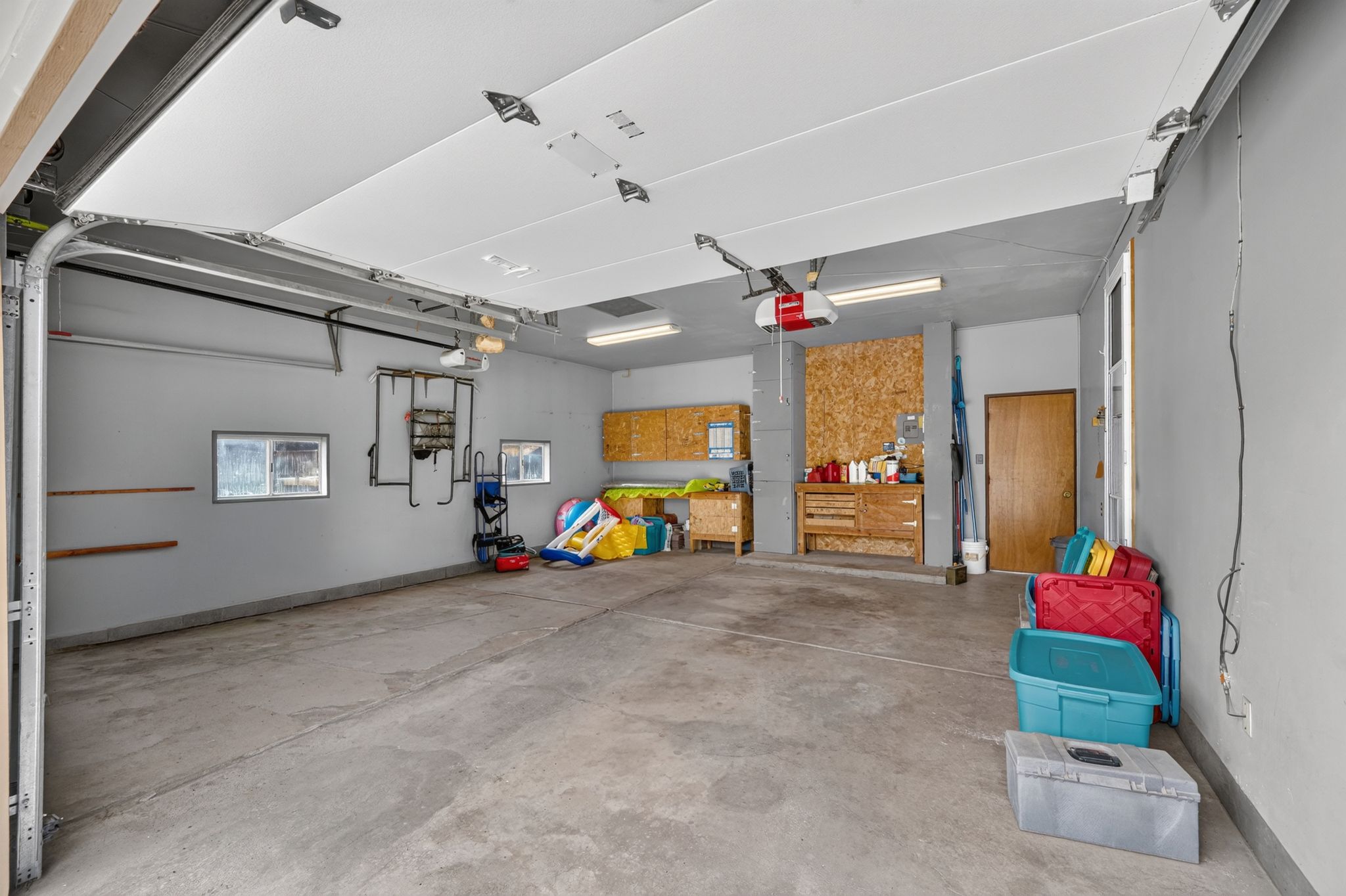 Spacious garage with concrete flooring, two windows, built-in shelving, and a wood-paneled workbench area