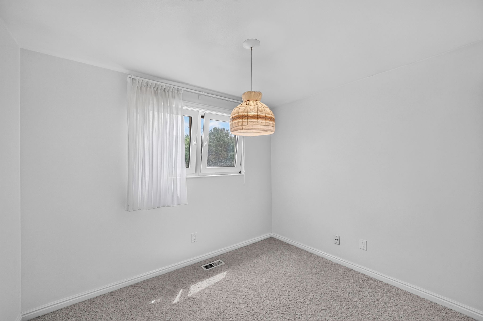 Bright room featuring a single window with a sheer curtain, a woven pendant light fixture, light gray carpet, and white baseboards