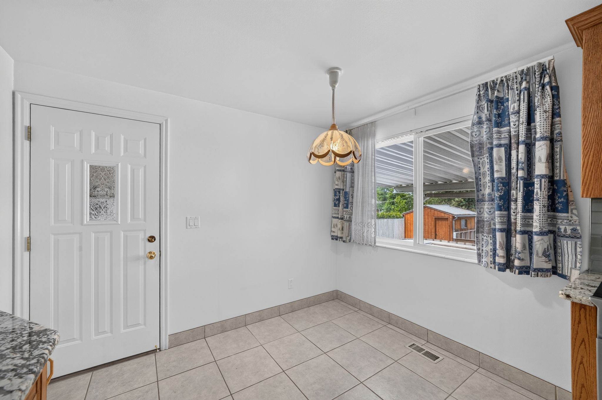 Bright interior space featuring a white paneled door with decorative glass, a window with exterior visibility, and an overhead light fixture