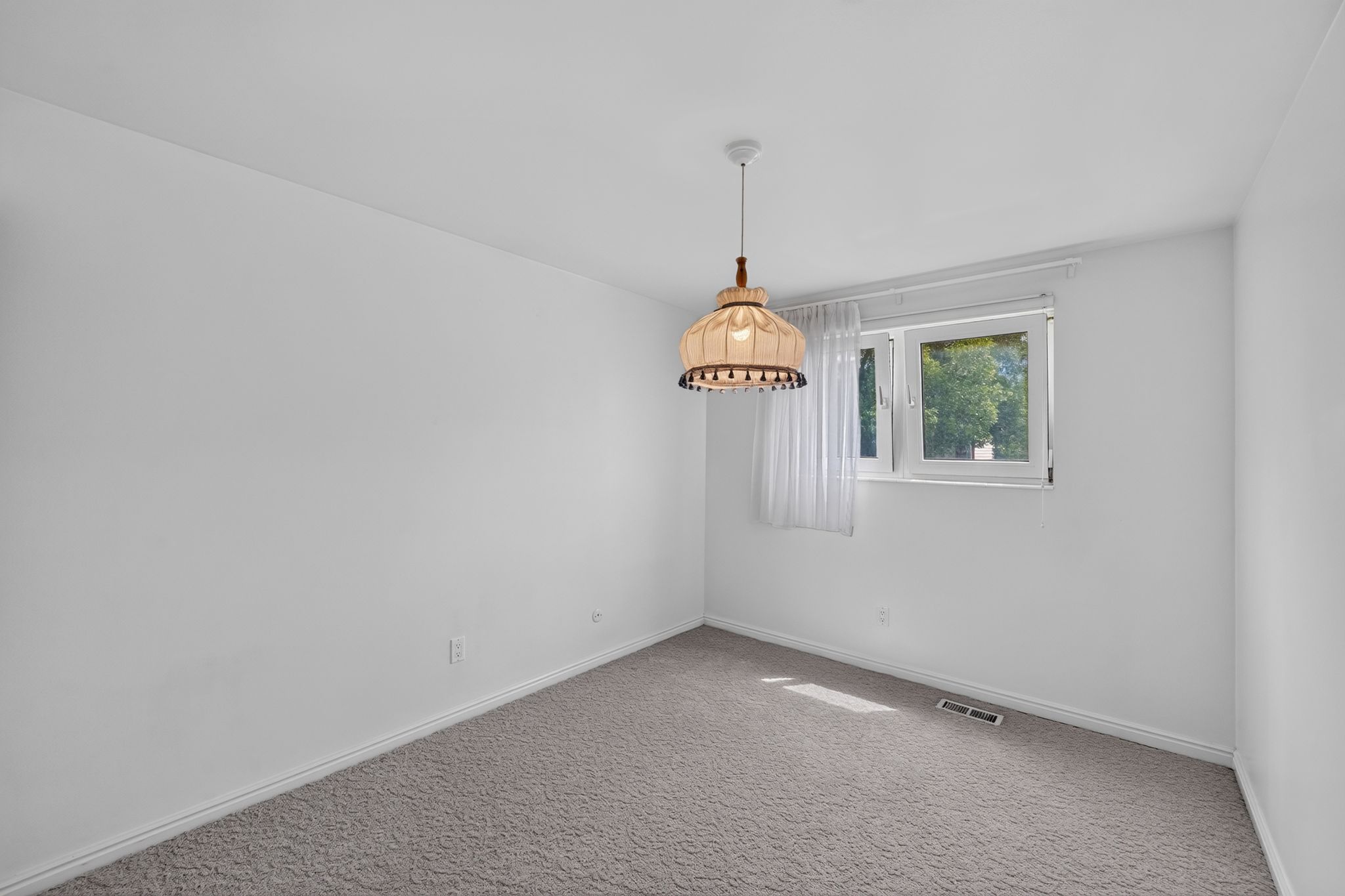 Room featuring neutral wall paint, gray carpet flooring, a window with exterior tree scenery, a ceiling-mounted pendant light, and white trim