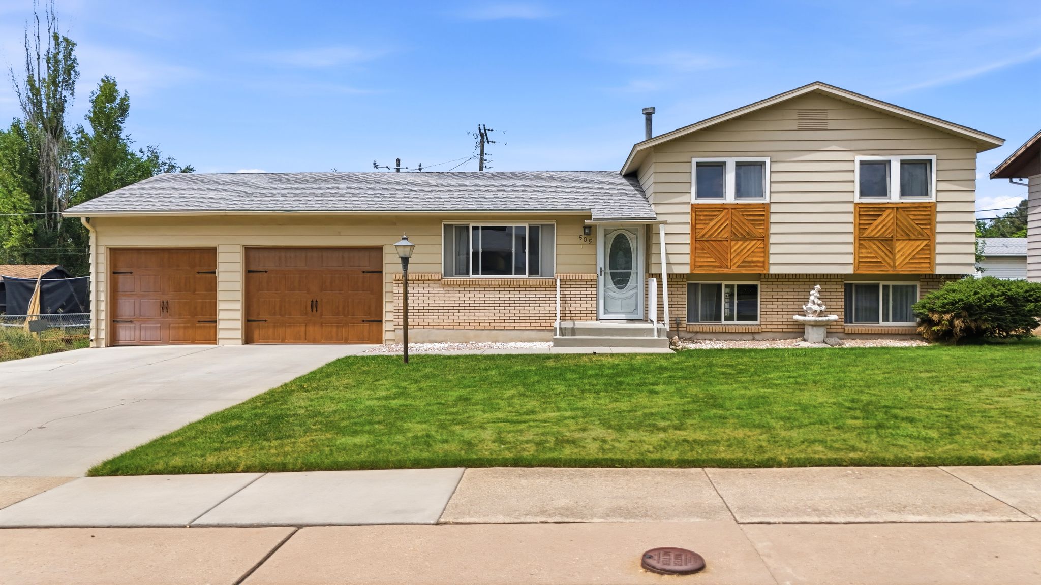 Split-level residence featuring a two-car garage with wood-finish doors, a concrete driveway, and a manicured front lawn