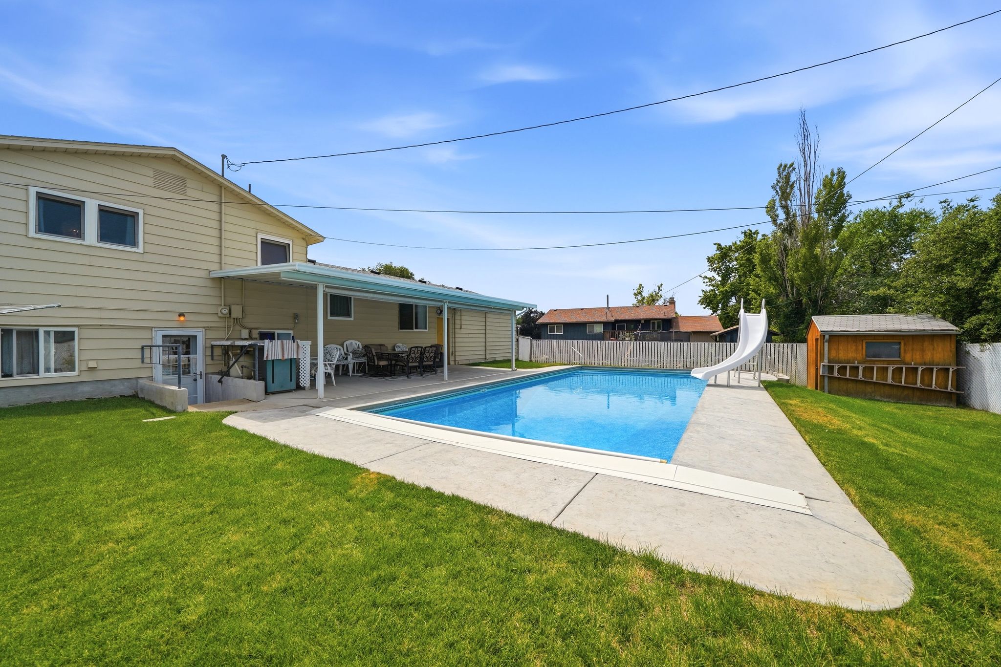 Expansive backyard featuring a rectangular in-ground swimming pool, concrete decking, and a covered patio area
