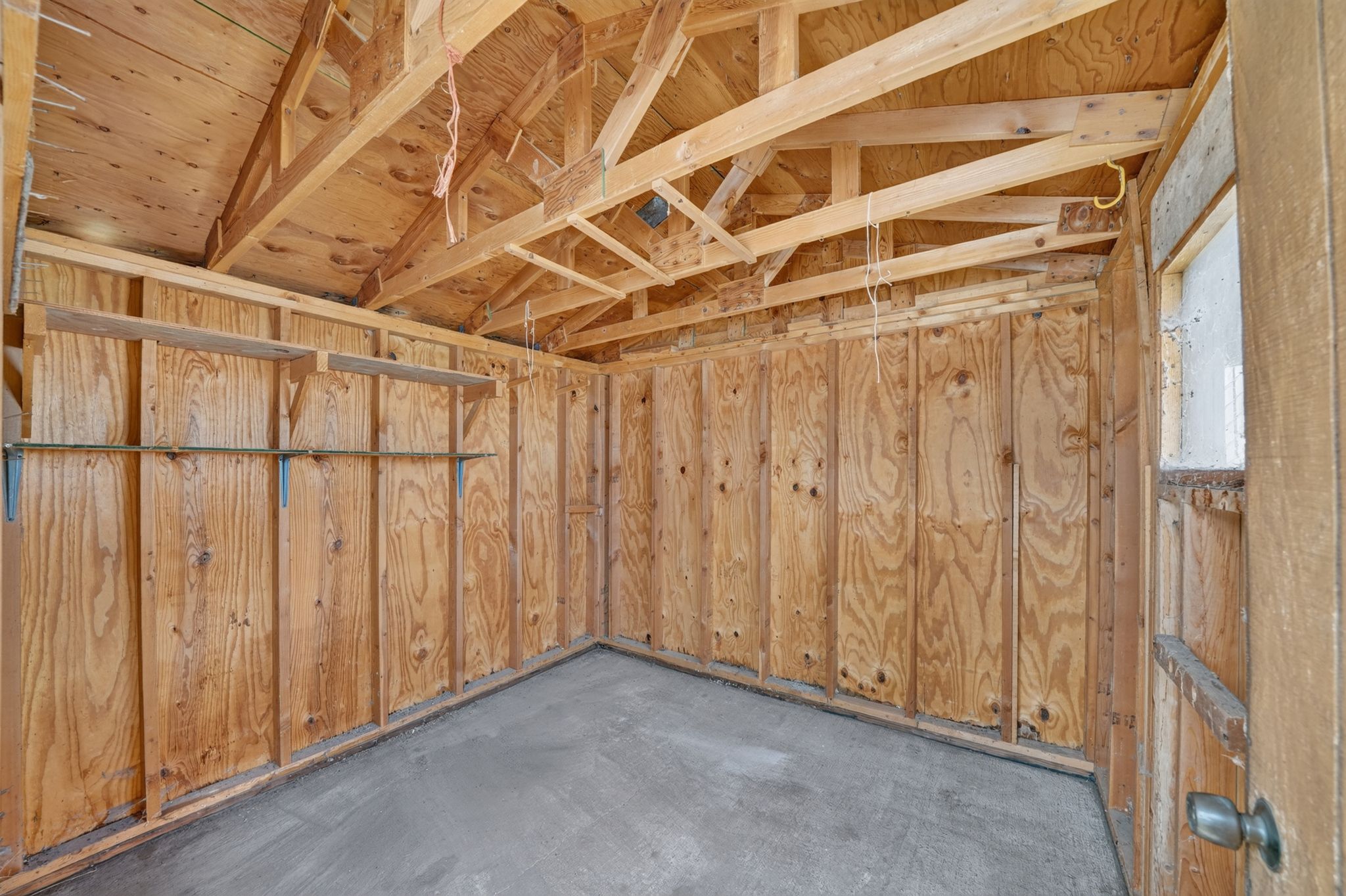 Unfinished interior space featuring exposed wood framing, plywood wall panels, a concrete floor, and a window with natural light