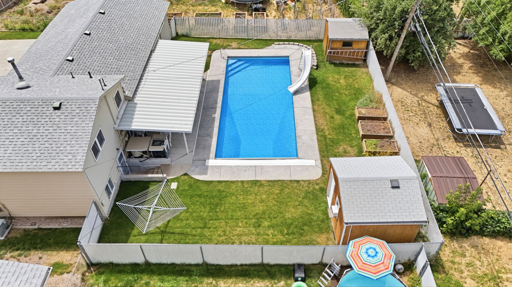 Fenced backyard featuring an in-ground swimming pool with a slide, a covered patio area, and two additional storage sheds