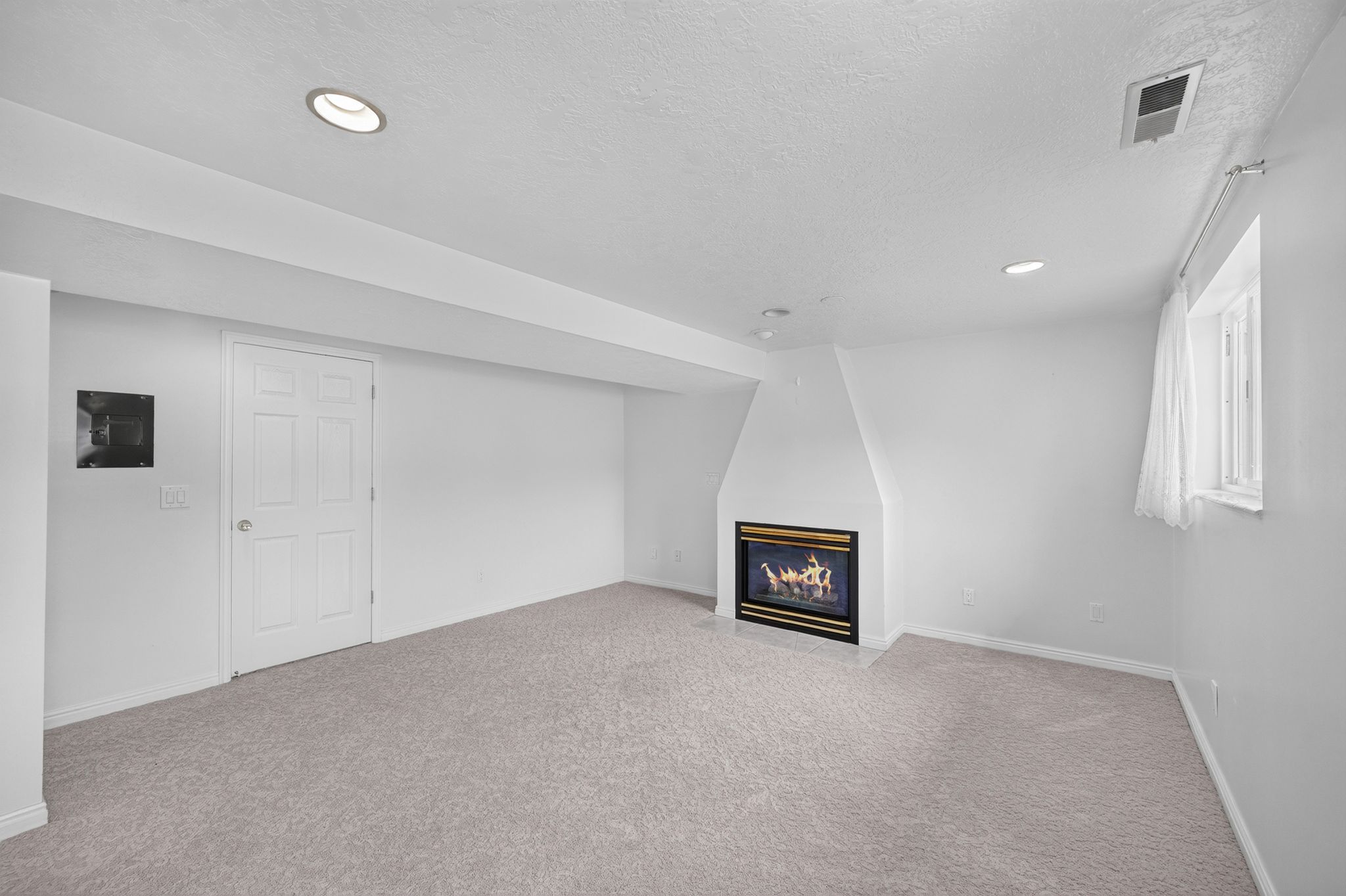 Carpeted room featuring a built-in fireplace with a black and gold-tone surround, recessed lighting, and a multi-pane window