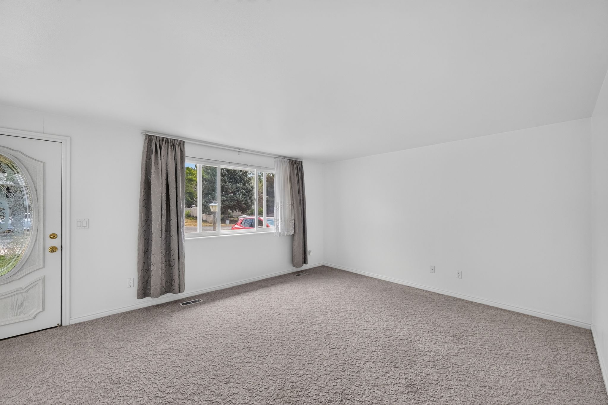 Bright interior room featuring a decorative glass paneled entry door, neutral wall paint, and gray textured carpeting