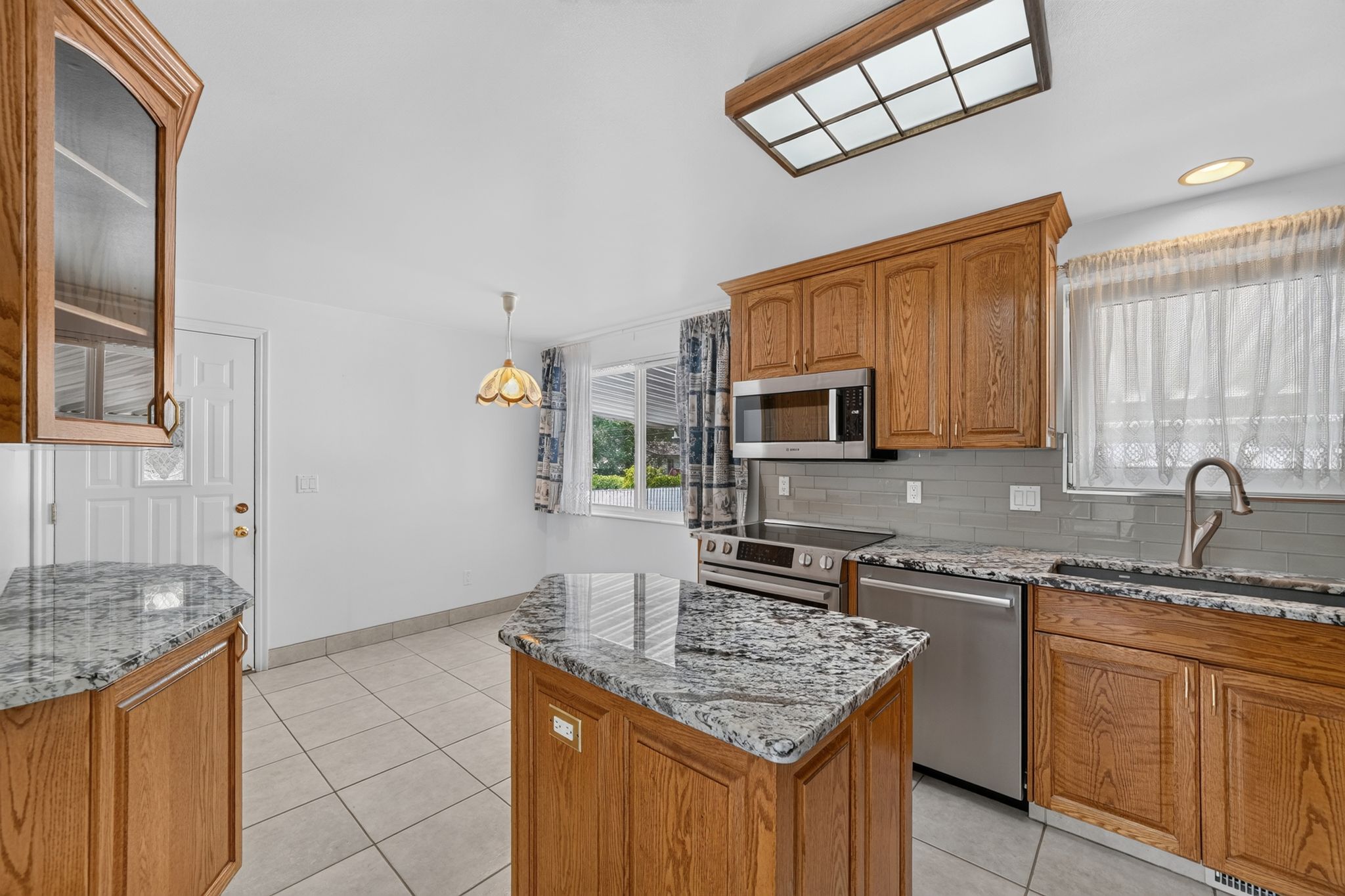 Kitchen featuring a center island, tile flooring, wood cabinetry, stainless steel appliances, and stone-finish countertops
