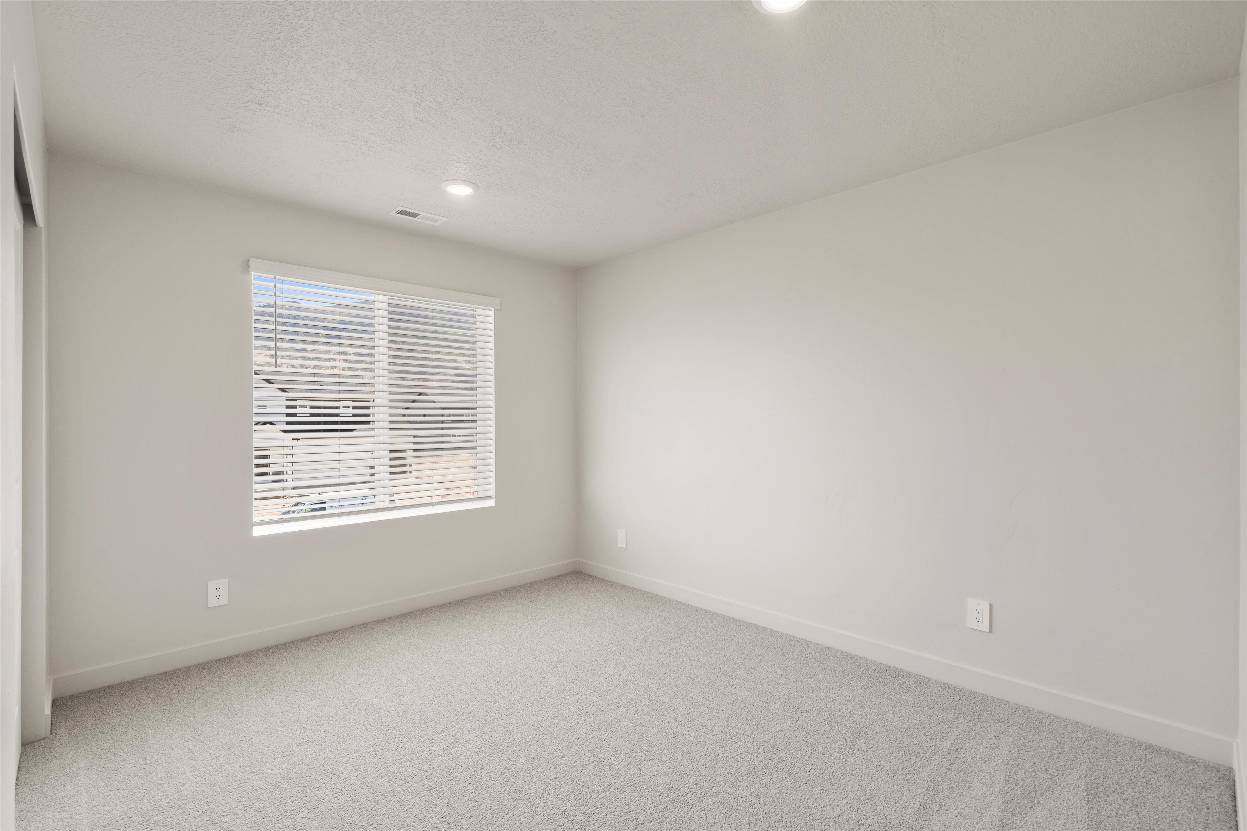 Bright interior room featuring a large window with blinds, recessed ceiling lighting, light gray wall paint, and gray carpeting