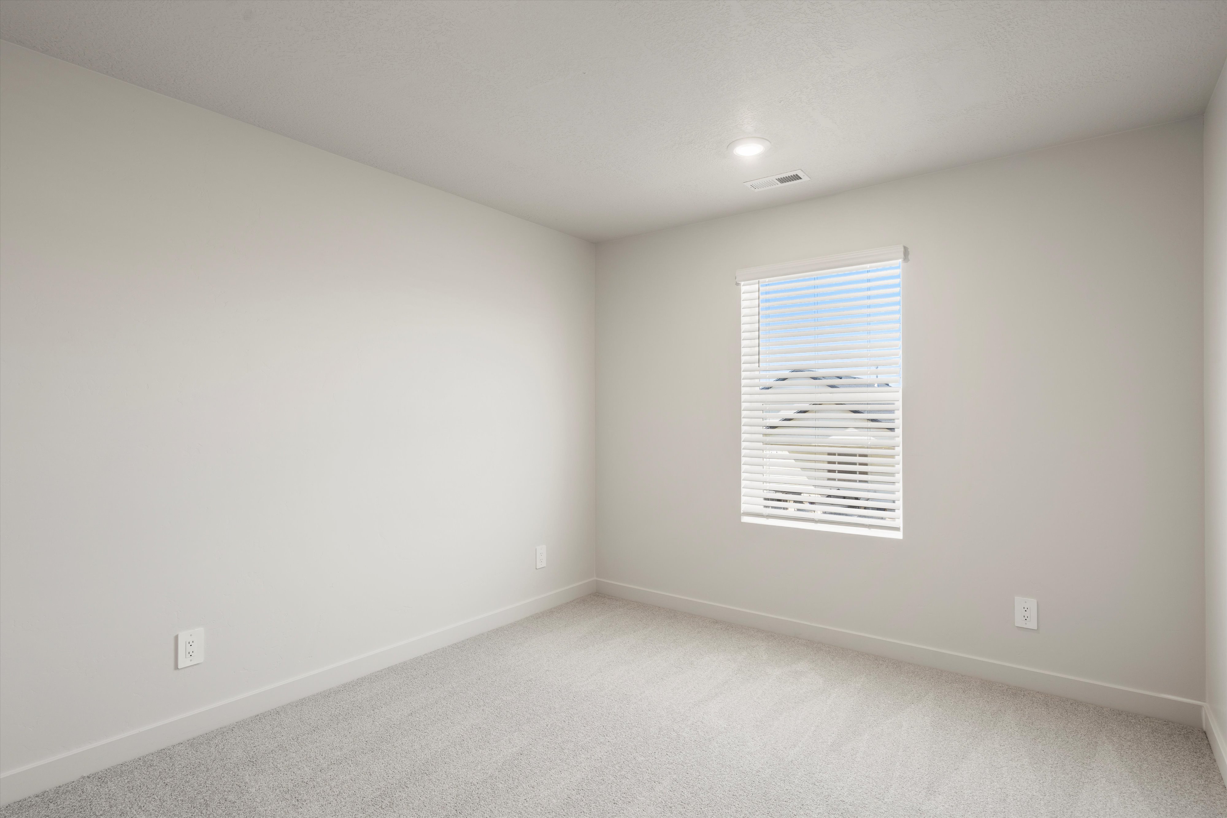 Bright room featuring a window with horizontal blinds, neutral wall paint, light gray carpeting, and recessed lighting