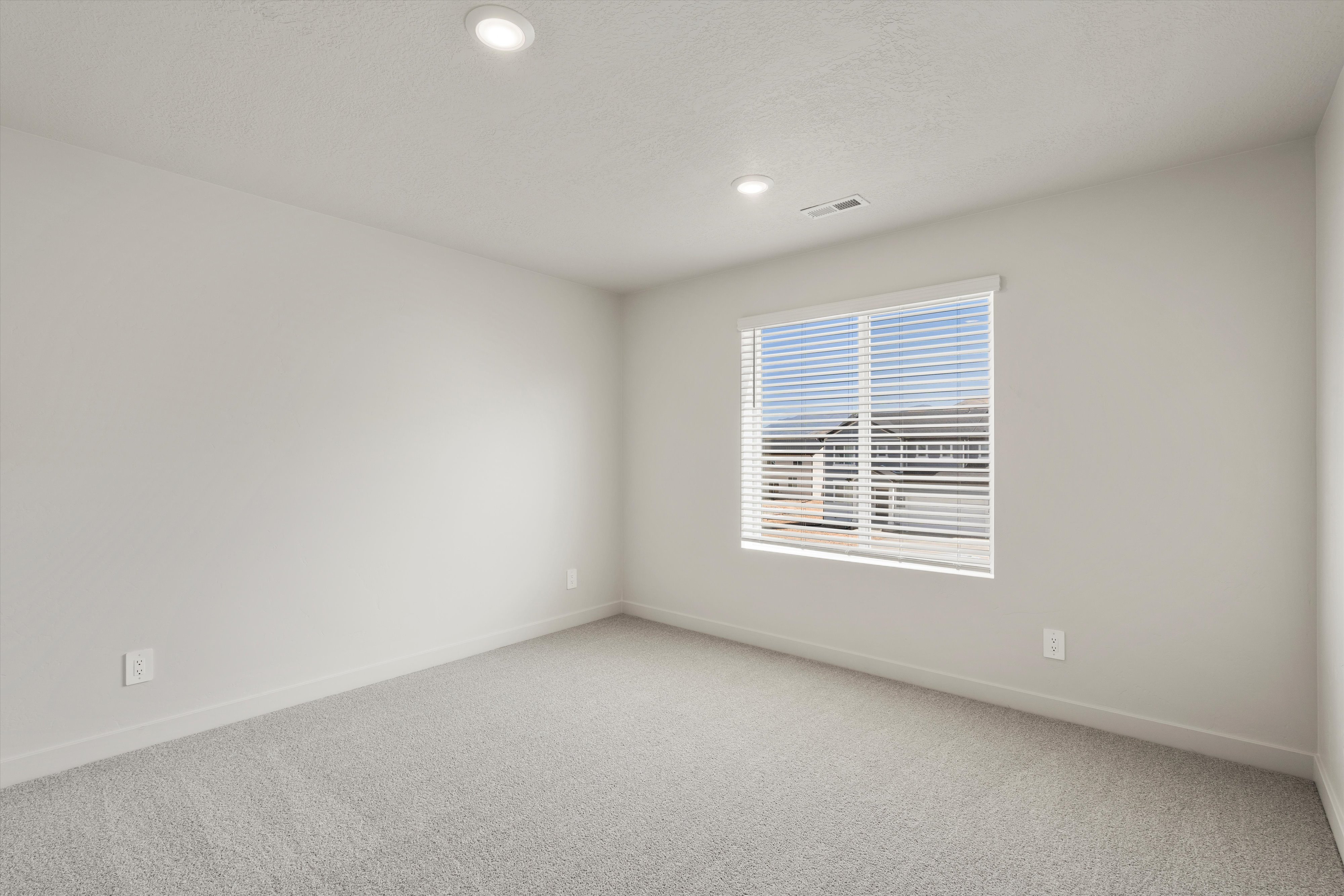Recessed lighting fixtures, broad window with horizontal blinds, and light-toned carpeting