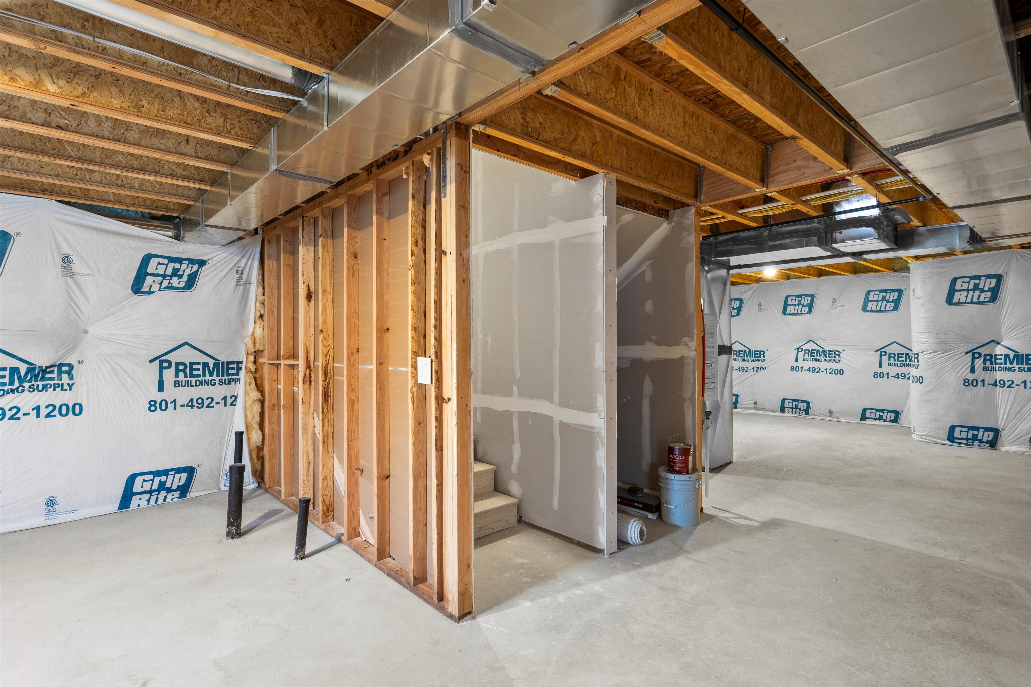 Unfinished basement area featuring exposed wood joists, structural framing, ductwork, and partial drywall installation around a staircase