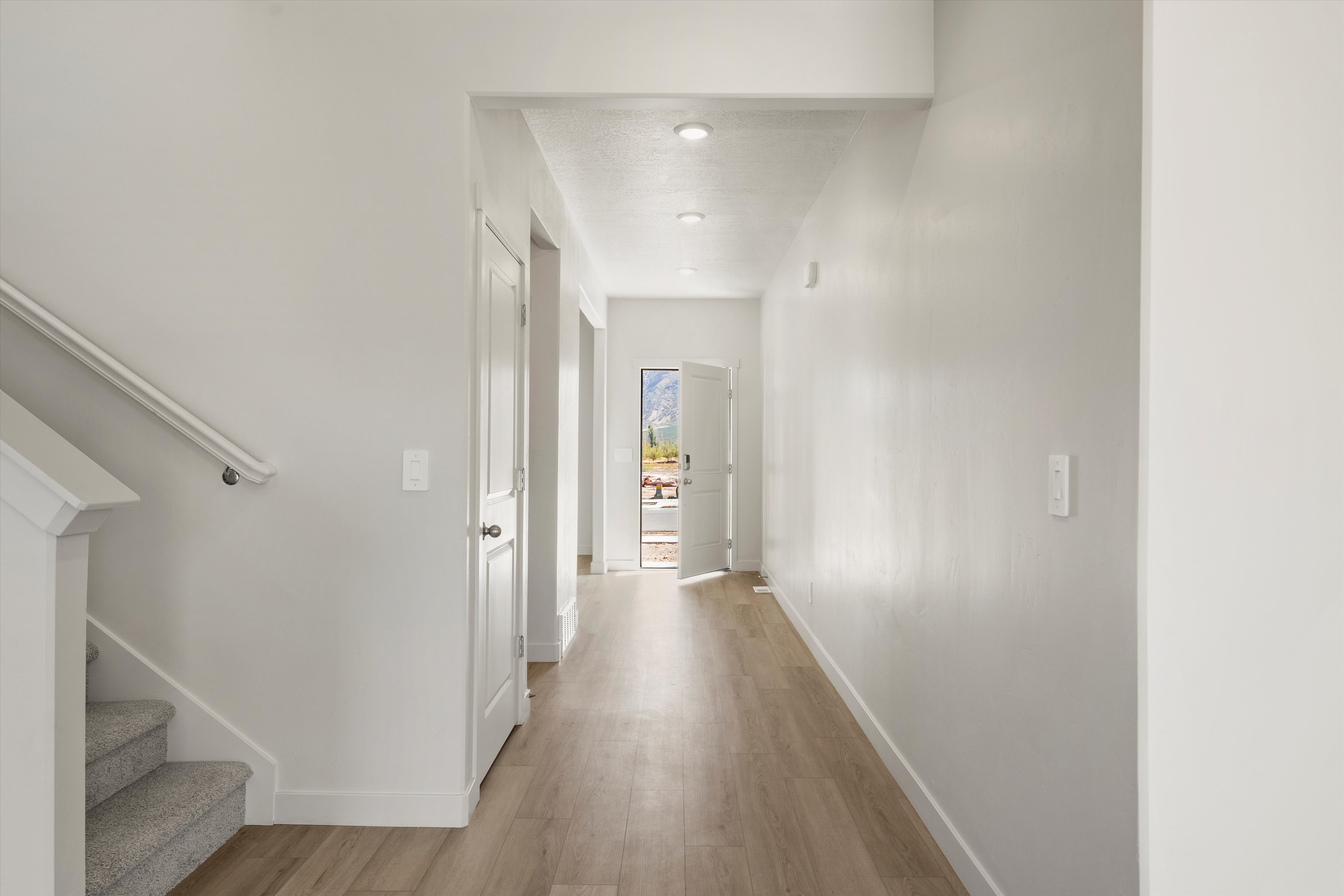 Entryway hall featuring light wood-finish flooring, recessed lighting, and a staircase with neutral carpet and a white banister