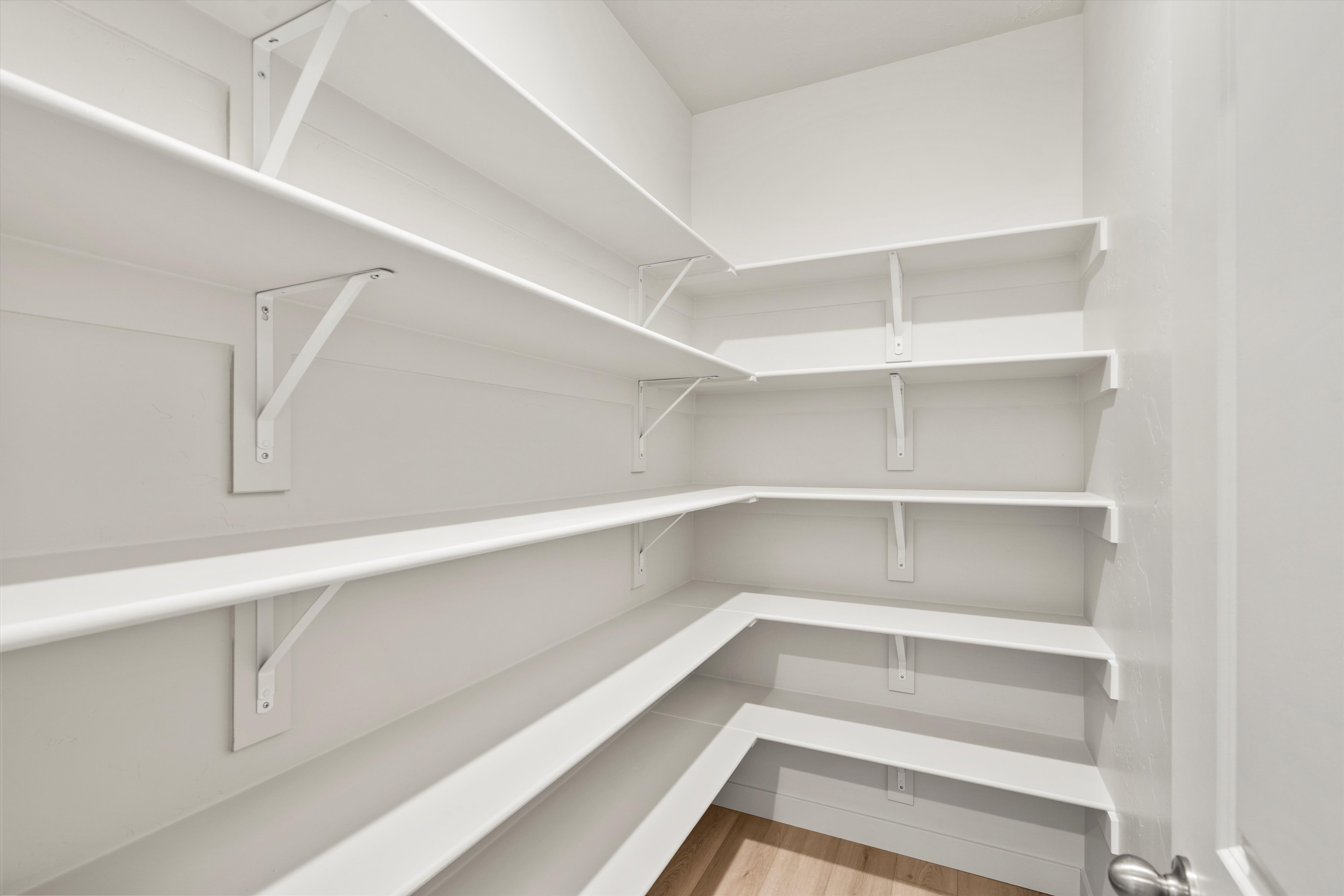 Walk-in pantry featuring white shelving, L-shaped configurations, and wood-finish flooring