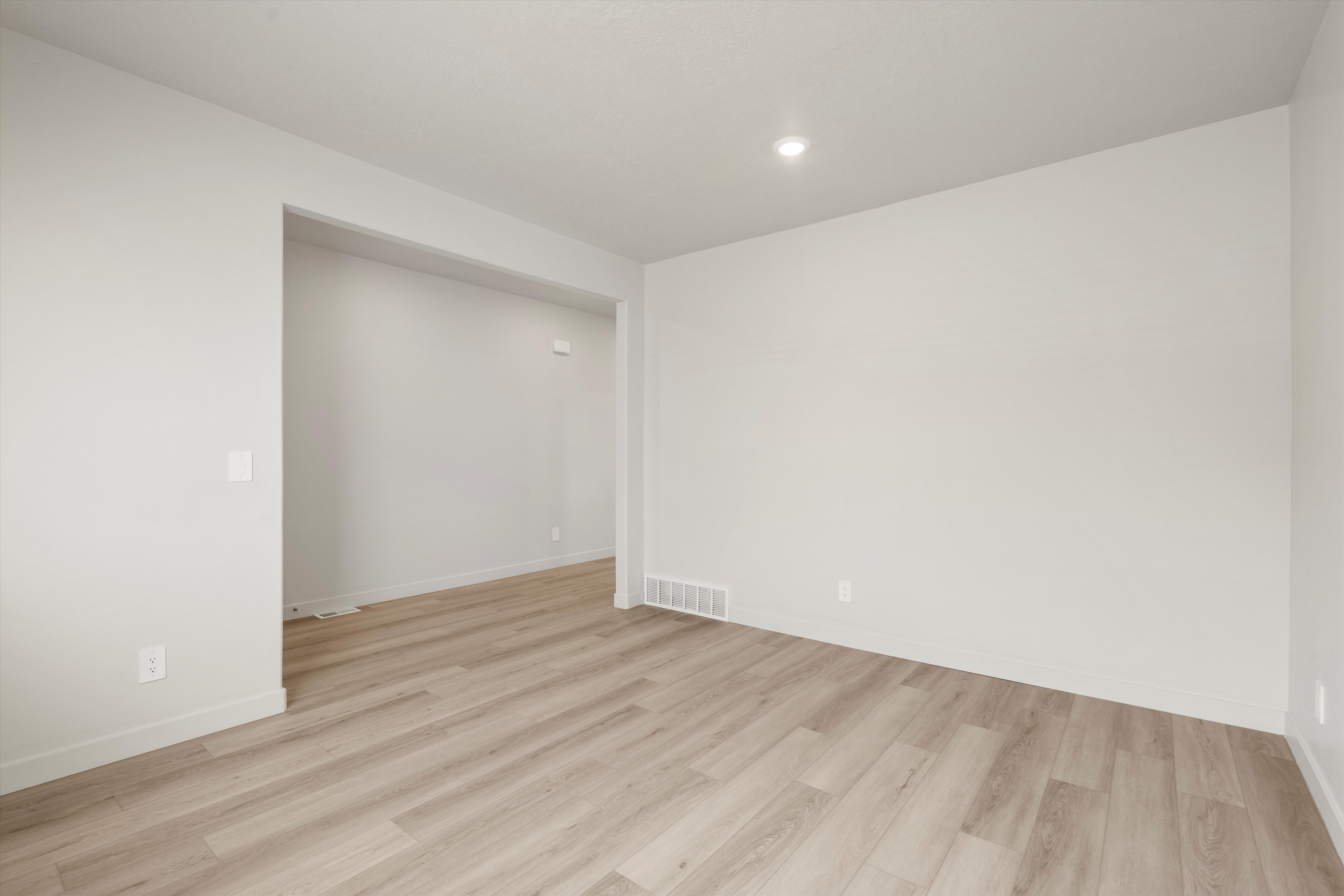 Spacious room featuring light wood-finish flooring, recessed ceiling lighting, and crisp white walls