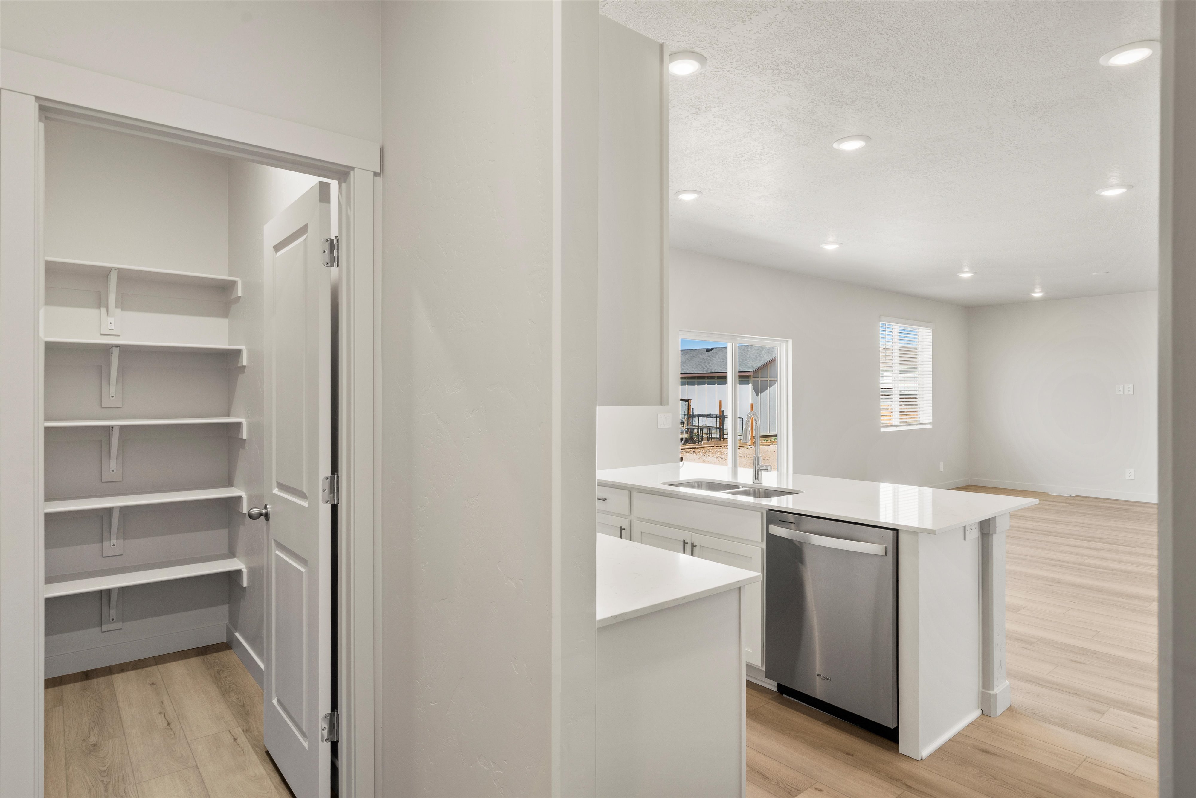 Walk-in pantry with ample shelving, positioned conveniently to a modern kitchen featuring white cabinetry, quartz countertops, a stainless steel dishwasher, and an undermount sink with a gooseneck faucet
