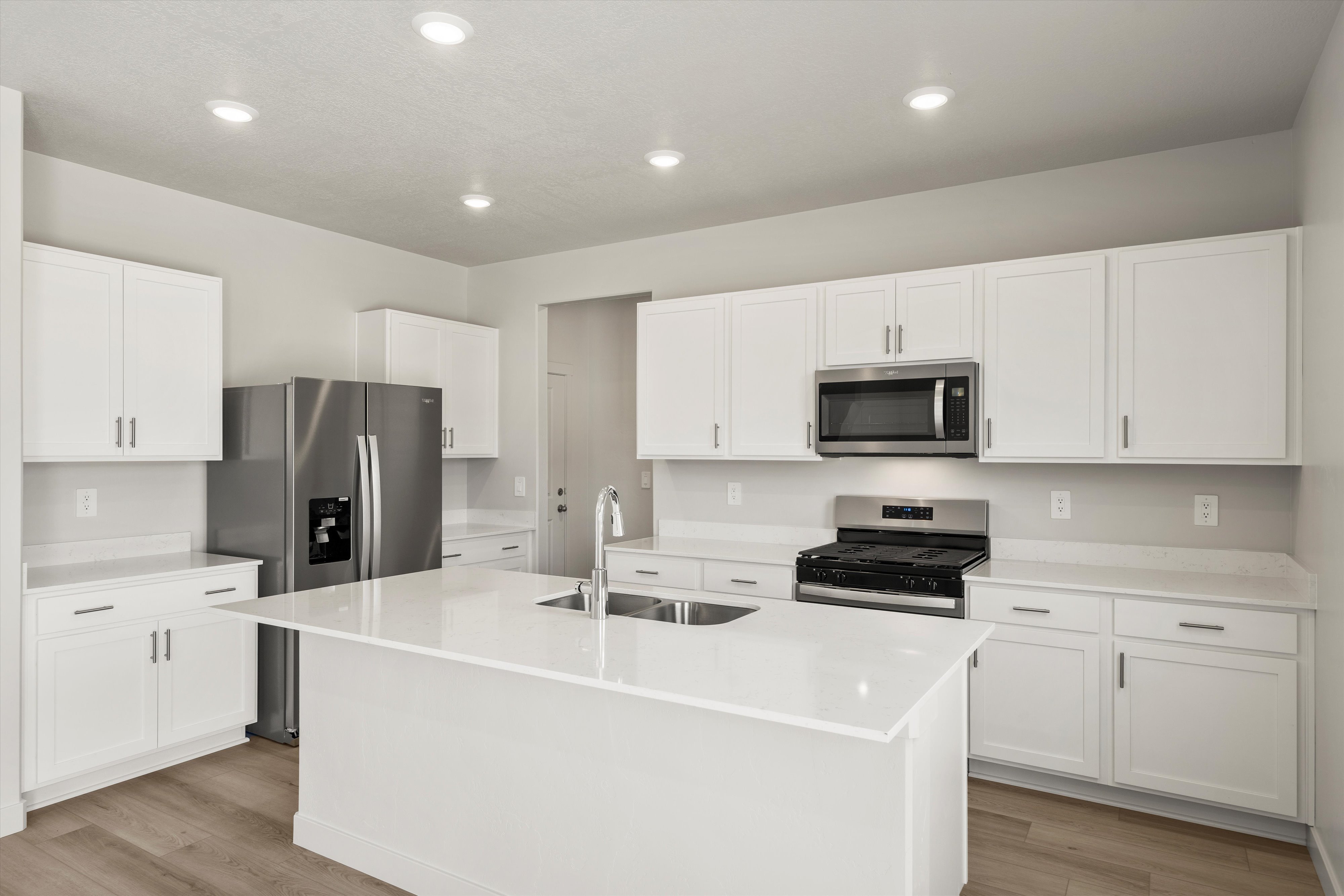 Modern kitchen featuring white shaker cabinetry, stainless steel appliances, a center island with an undermount sink, recessed lighting, and wood-finish flooring