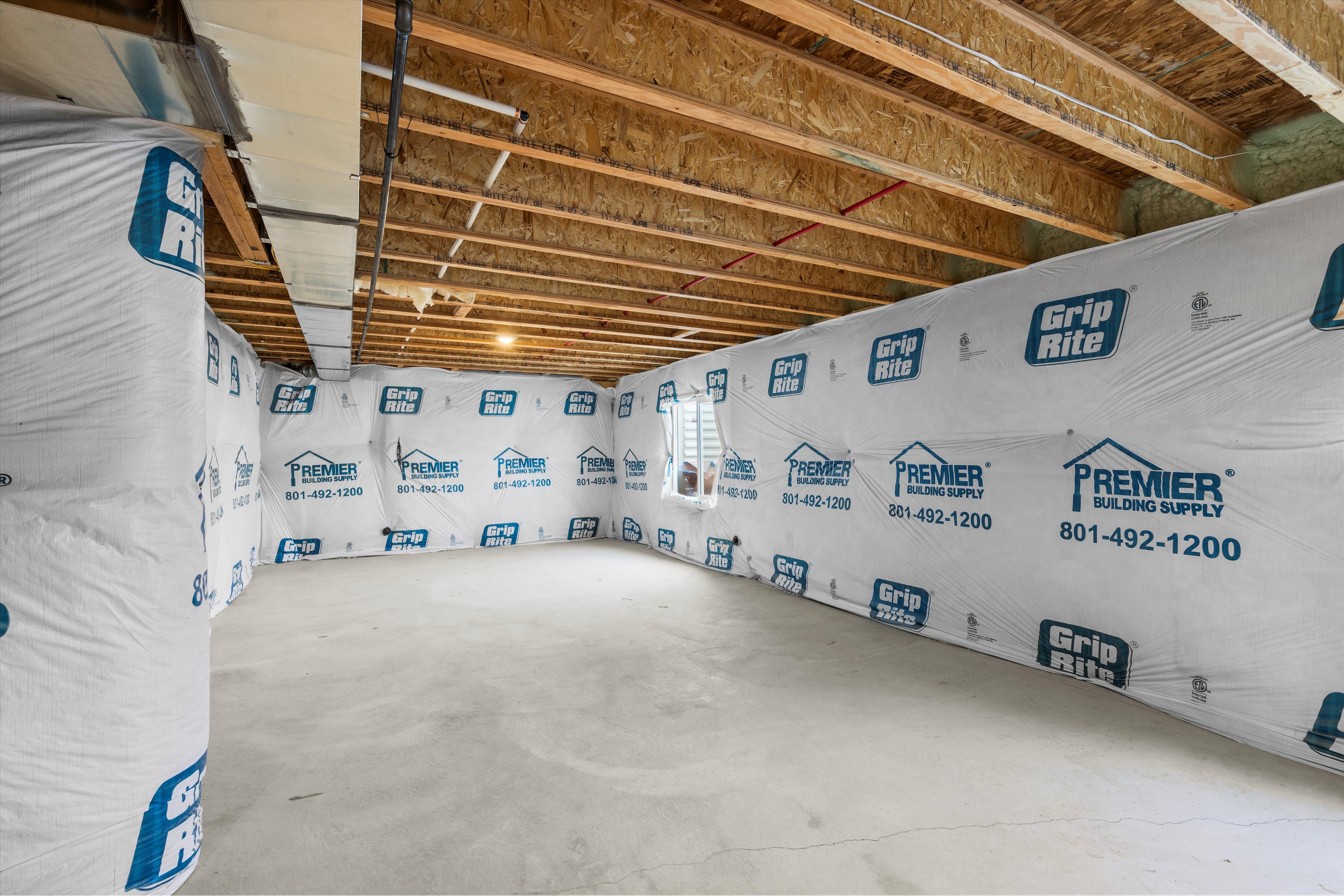 Unfinished basement space featuring exposed wood joists, concrete flooring, and insulated walls