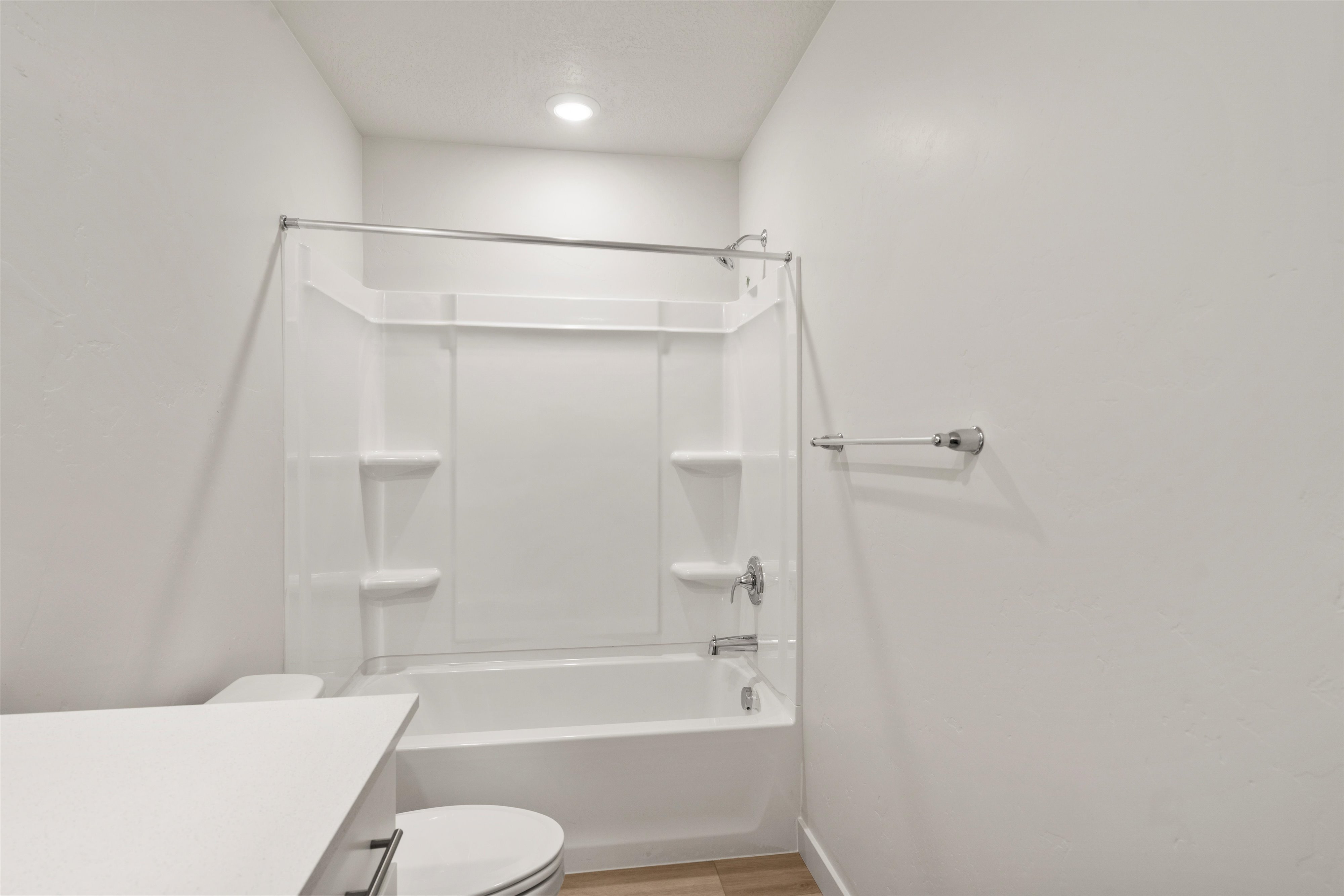White acrylic tub and shower combination with built-in shelving, chrome fixtures, and a curved shower rod