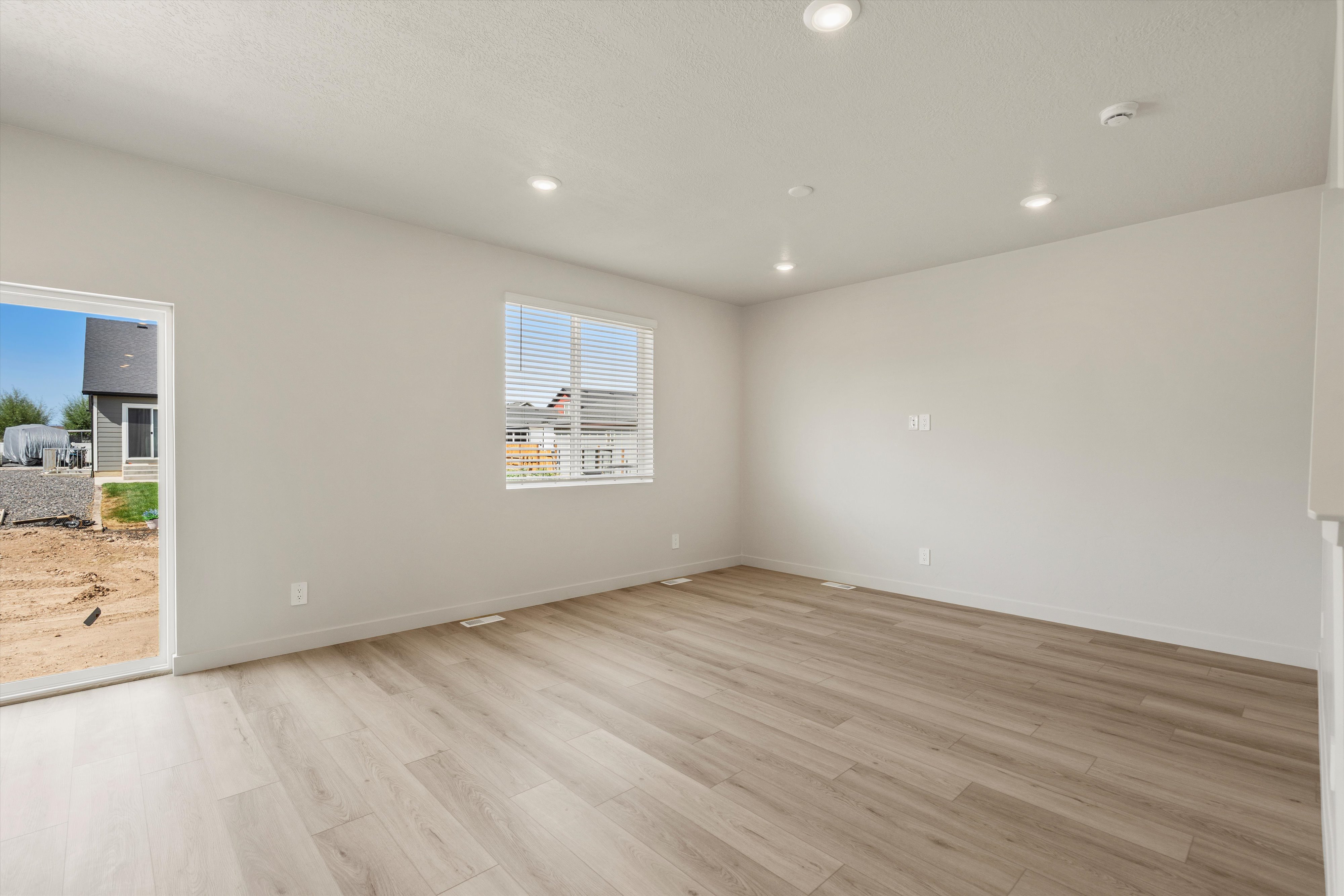 Spacious interior featuring light wood-finish flooring, recessed lighting, neutral wall paint, a window with blinds, and a sliding glass door