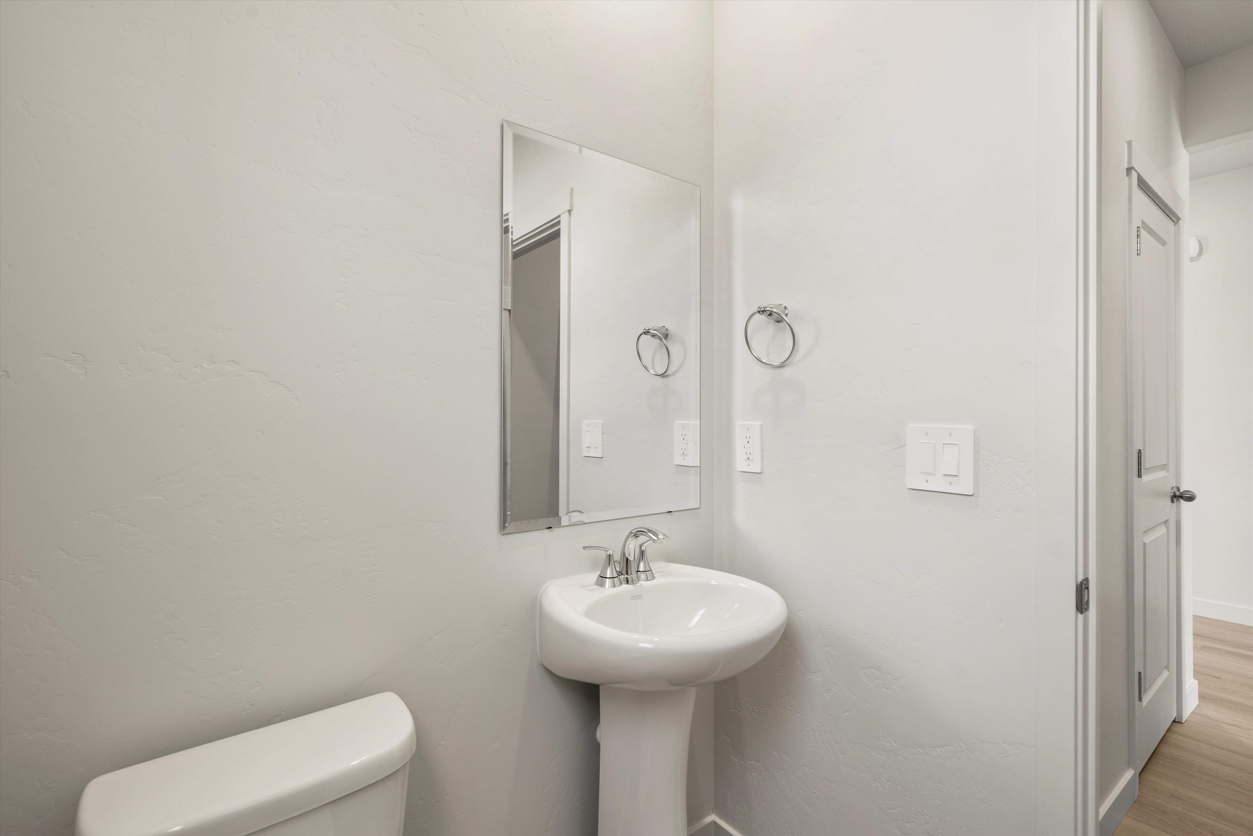 Pedestal sink with chrome faucet, complemented by a rectangular wall-mounted mirror