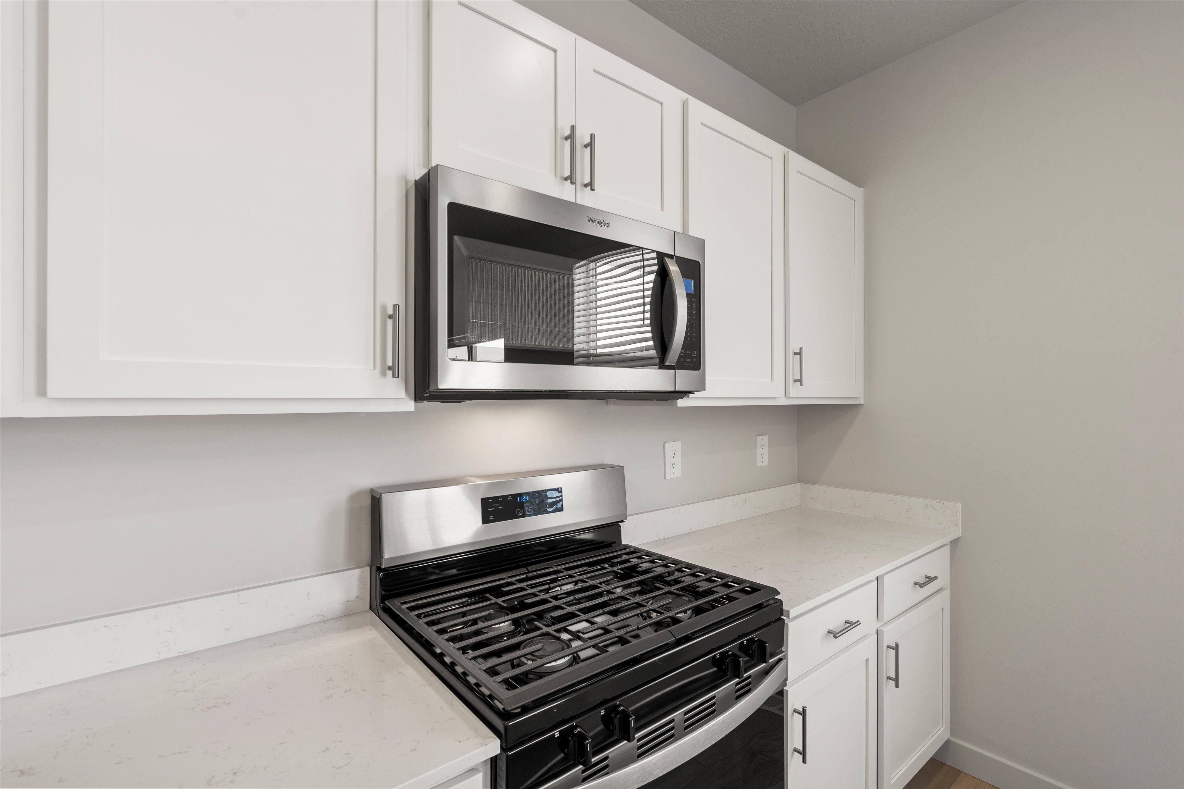 Contemporary kitchen featuring white shaker cabinetry, stainless steel microwave, gas range, and light-toned countertops