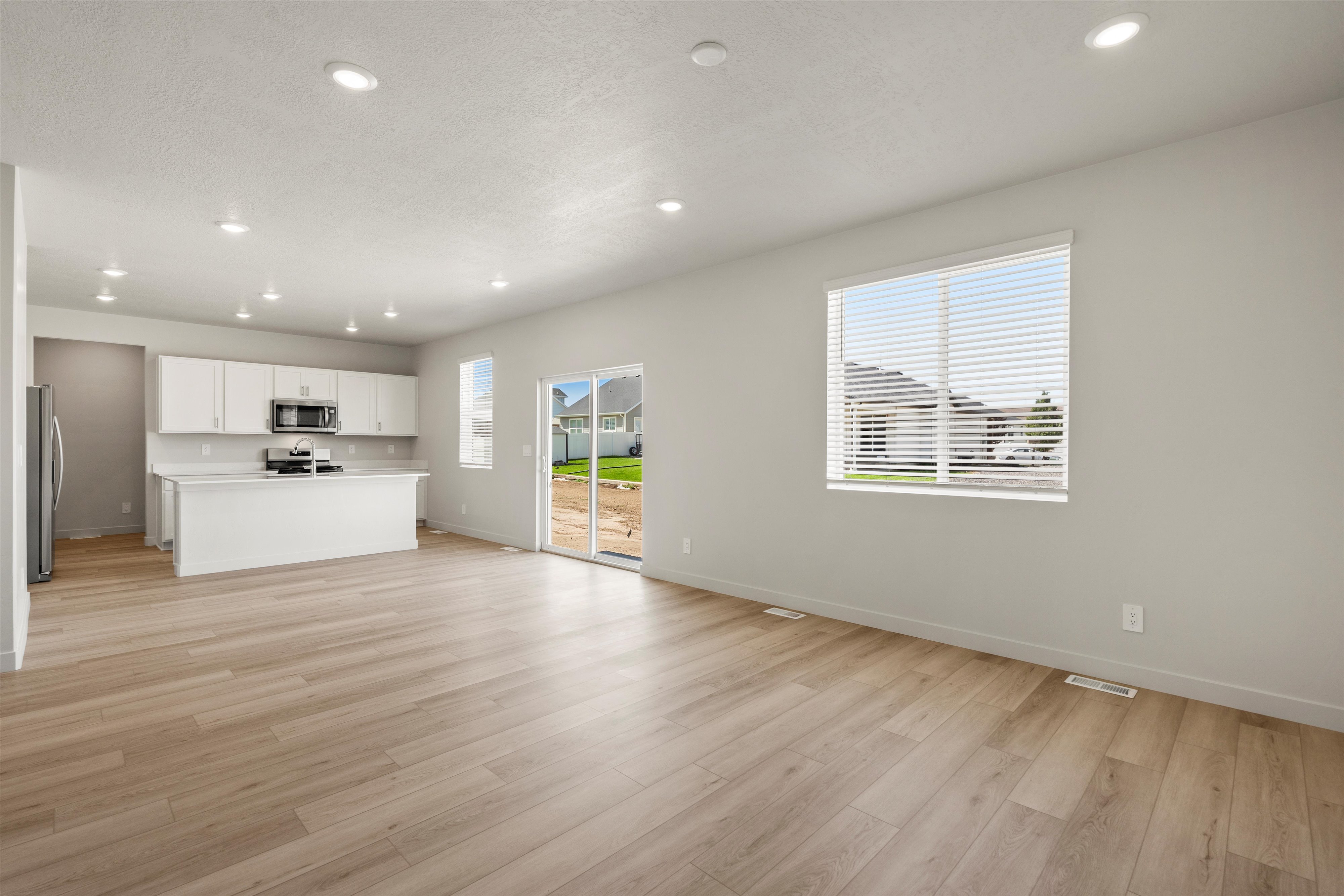 Open concept living space featuring wood-finish flooring, recessed lighting, and a modern kitchen with white cabinetry and stainless steel appliances