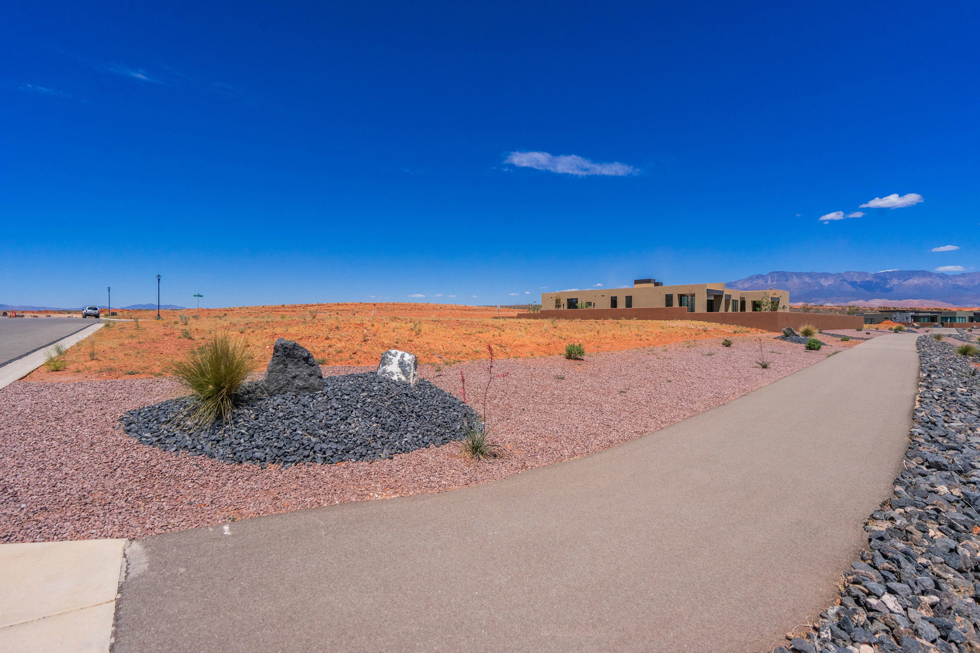 Expansive undeveloped land parcel with a paved pathway, desert landscaping, and distant mountain backdrop