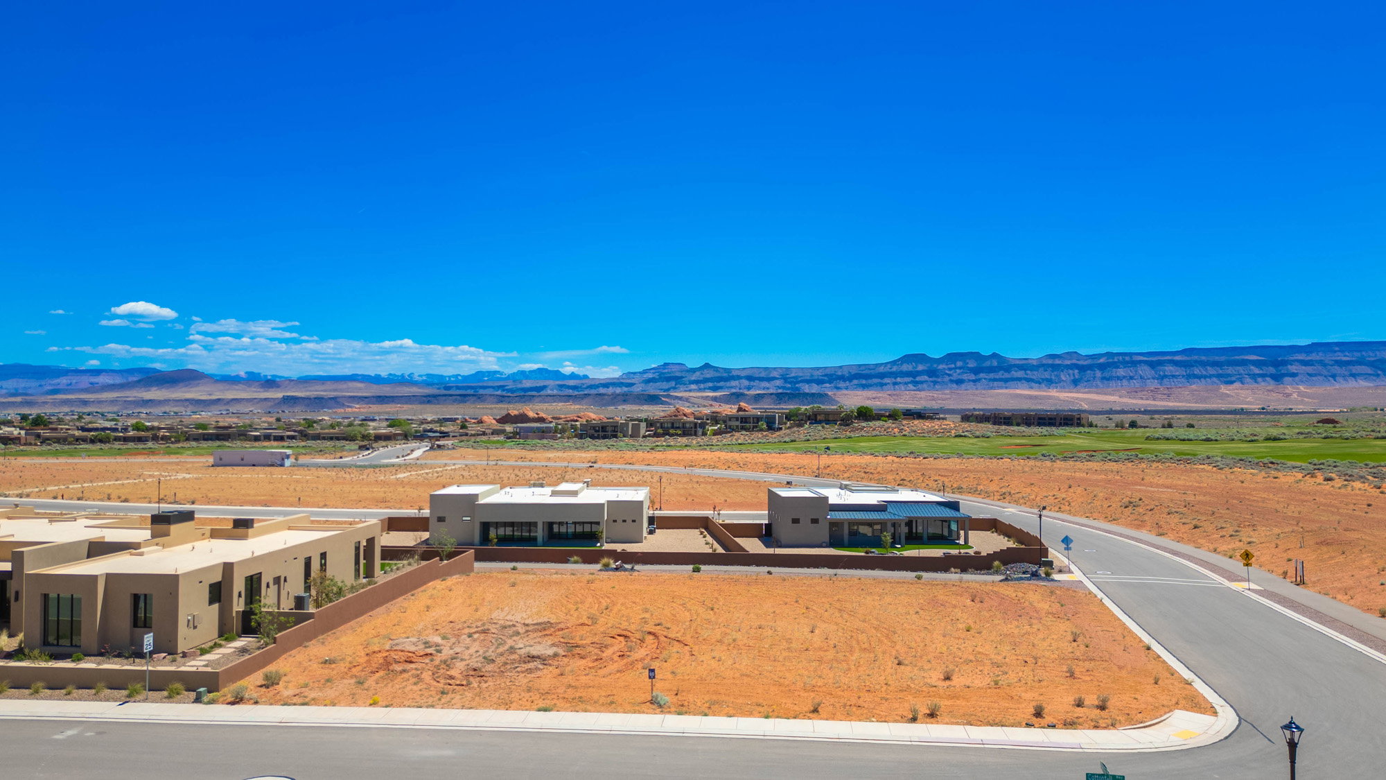Modern desert landscape featuring a paved road, developing residential properties, and distant mountains