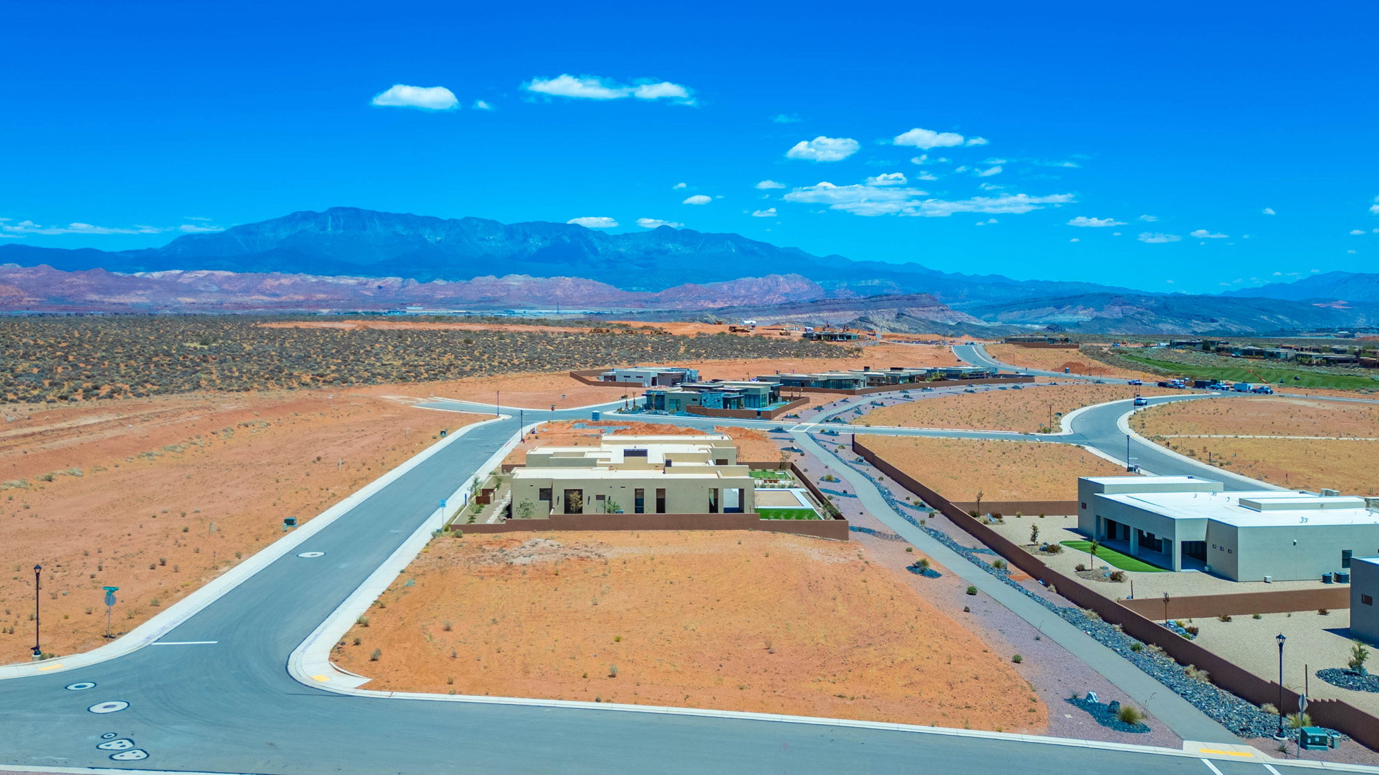 Expansive desert landscape with paved roadways, developing residential properties, distant mountains, and clear skies