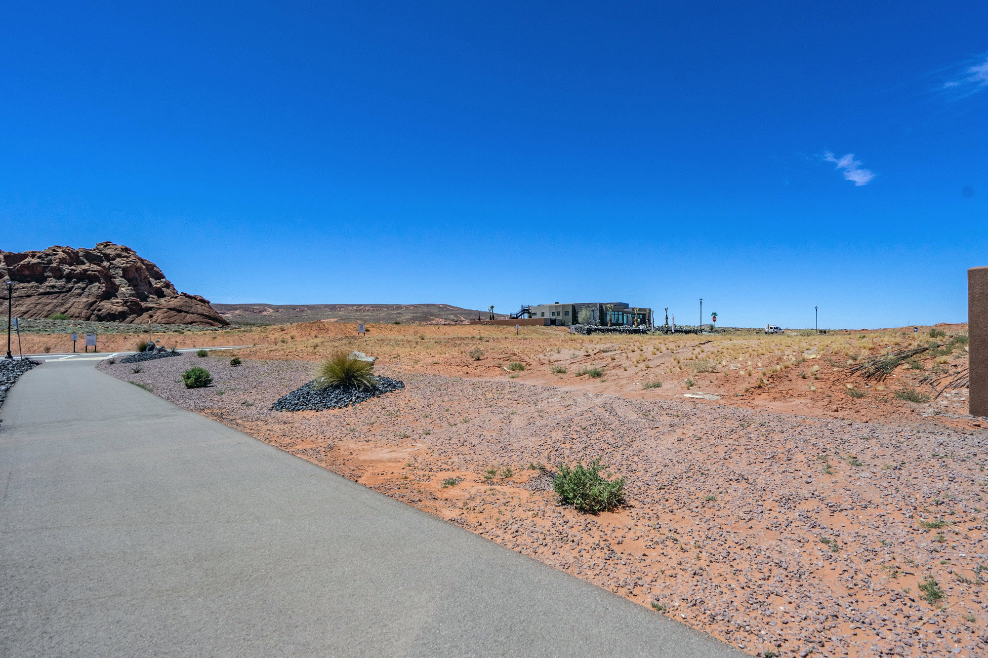 Paved pathway traversing arid terrain, with distant structures under a clear blue sky