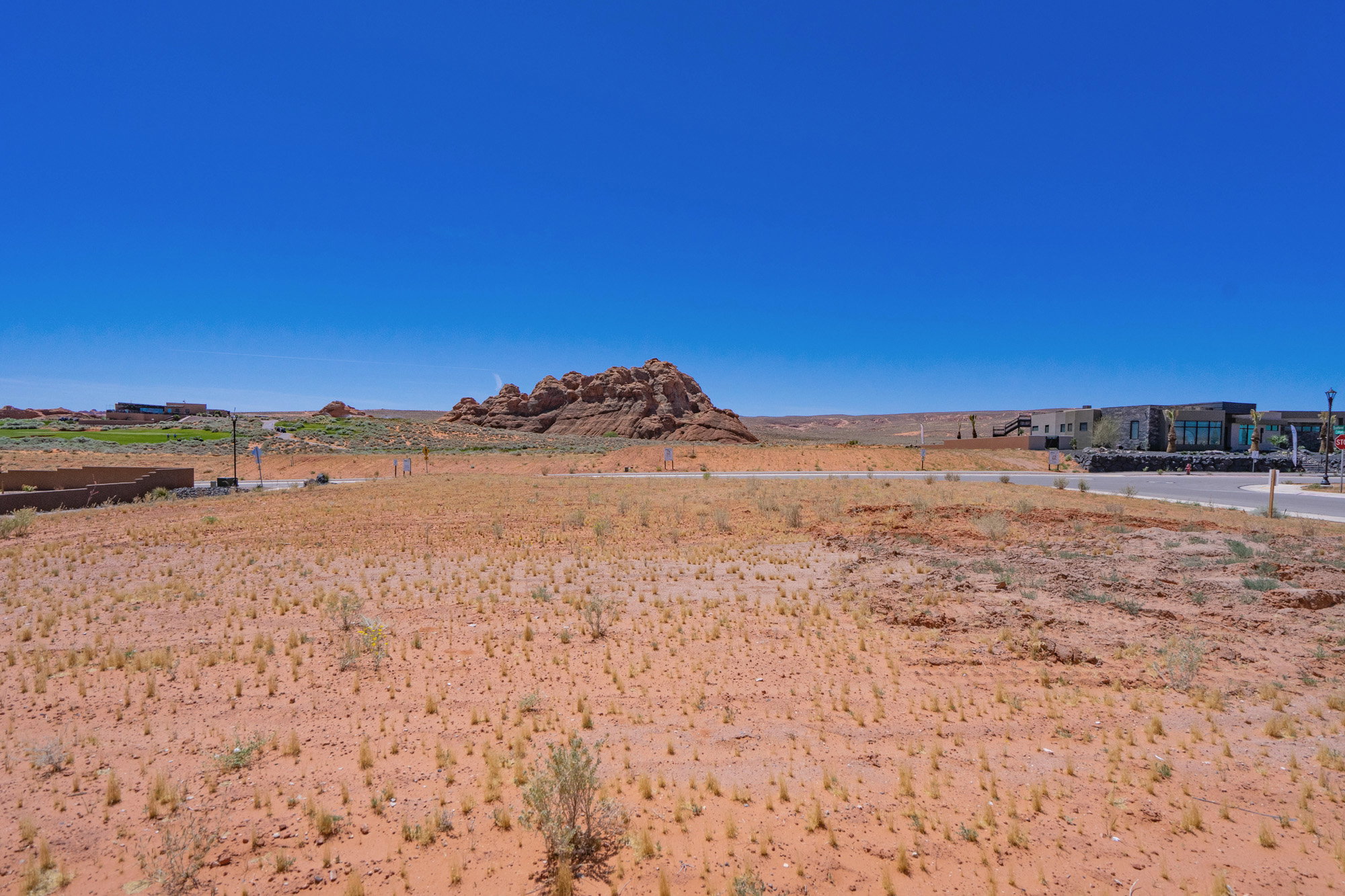 Expansive desert landscape featuring a clear blue sky, distant rock formations, and paved roadways