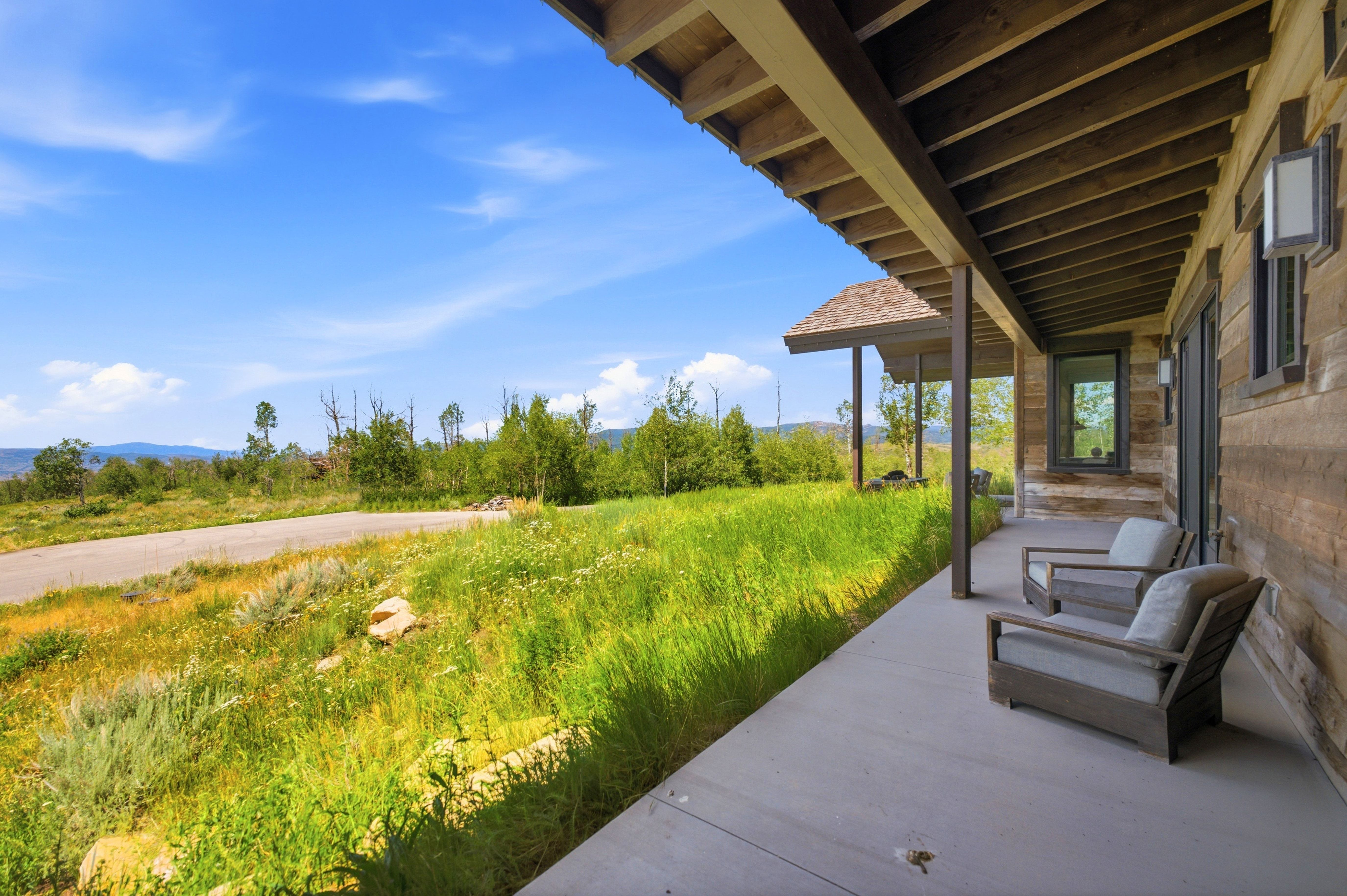 Expansive covered porch featuring a concrete surface, exposed wood beam ceiling, and rustic wood-paneled exterior