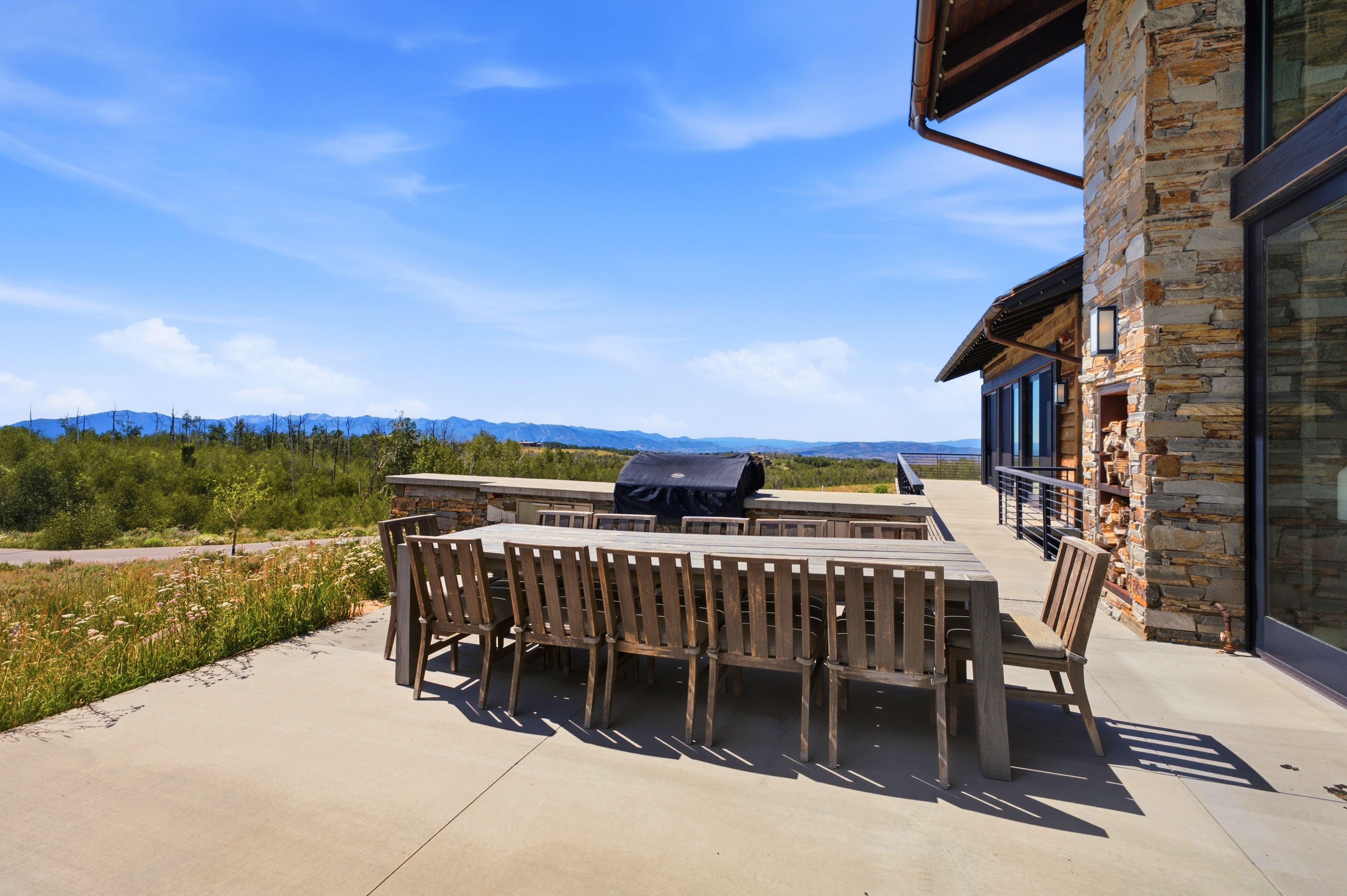 Expansive concrete patio with a built-in outdoor kitchen, stone accent wall, and a large sliding glass door