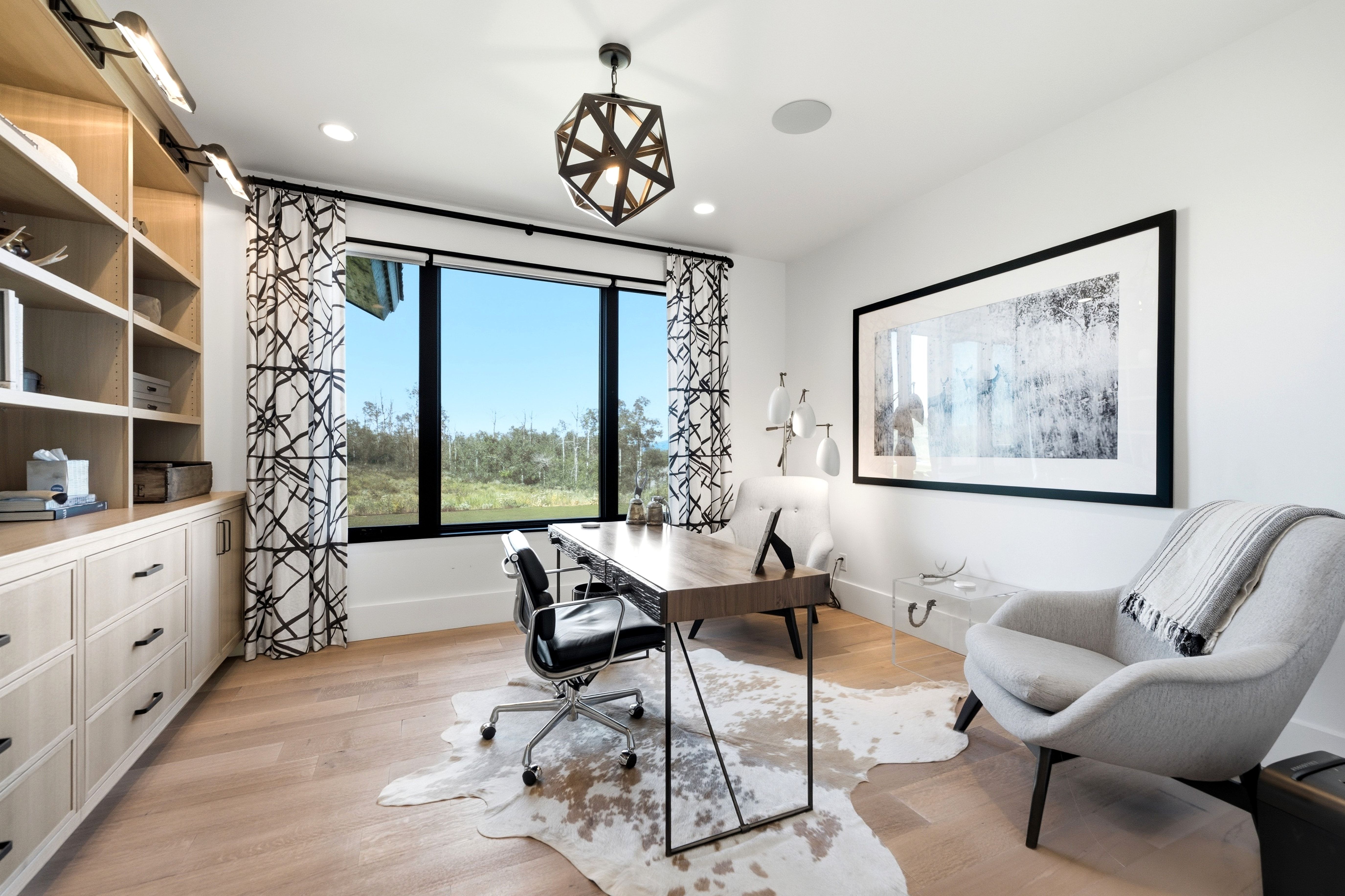 Spacious room featuring light wood-finish flooring, a large window with black trim, and a contemporary geometric light fixture