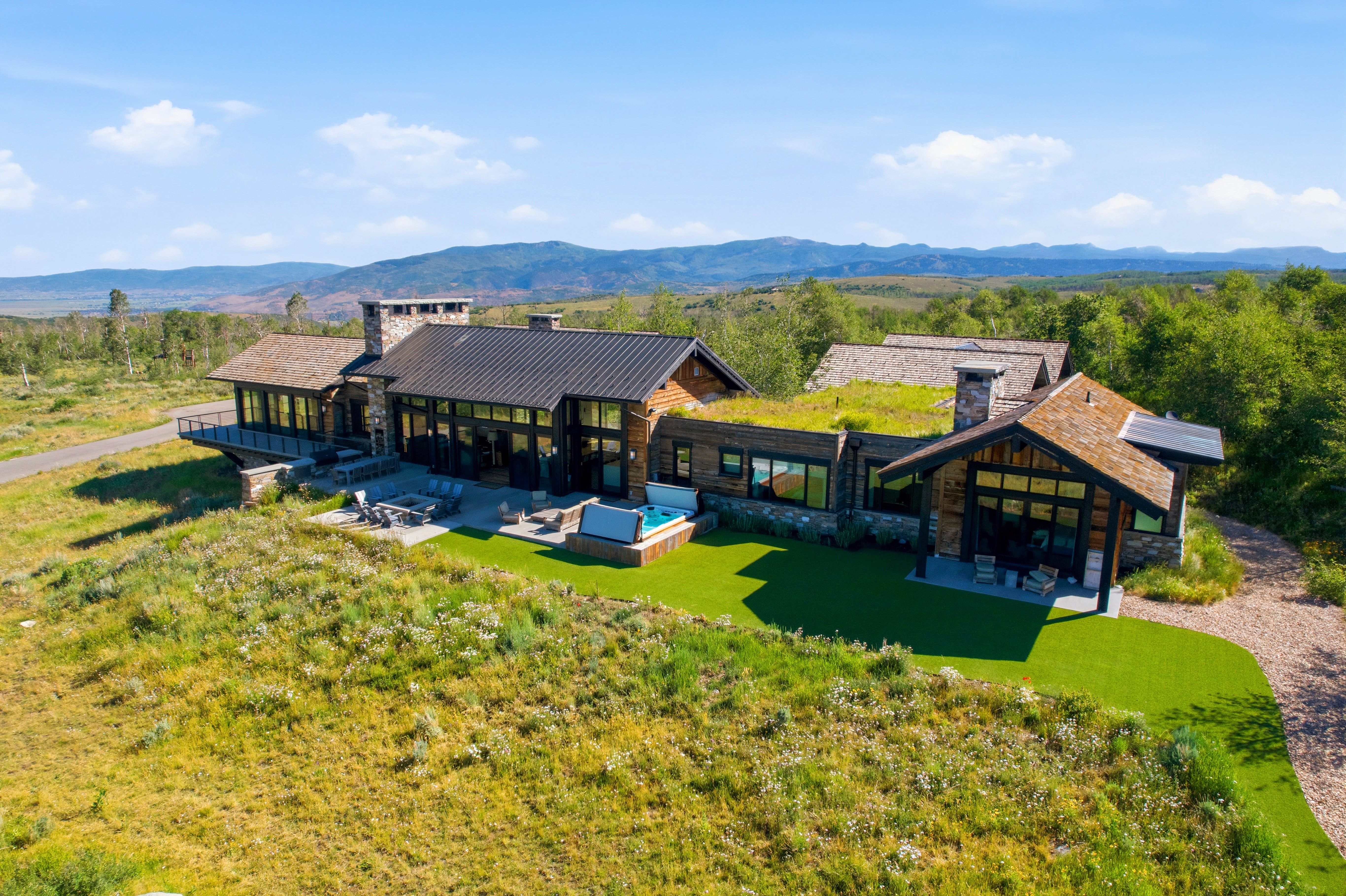 Modern mountain home featuring extensive glass facade, dark metal roofing, stone accents, and a green roof section