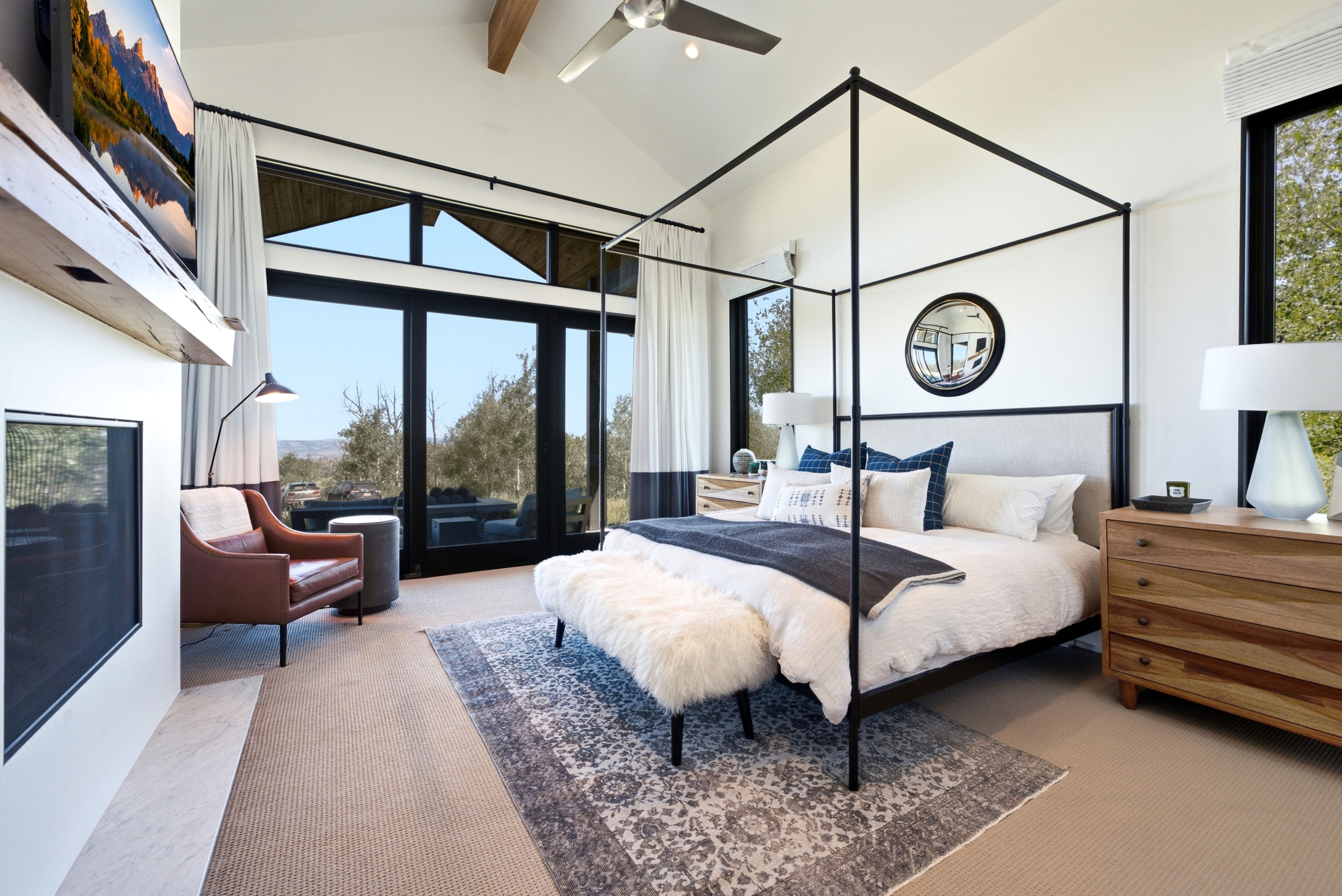 Bedroom featuring a vaulted ceiling with exposed wood beam, large black-framed windows, built-in fireplace, and integrated ceiling fan