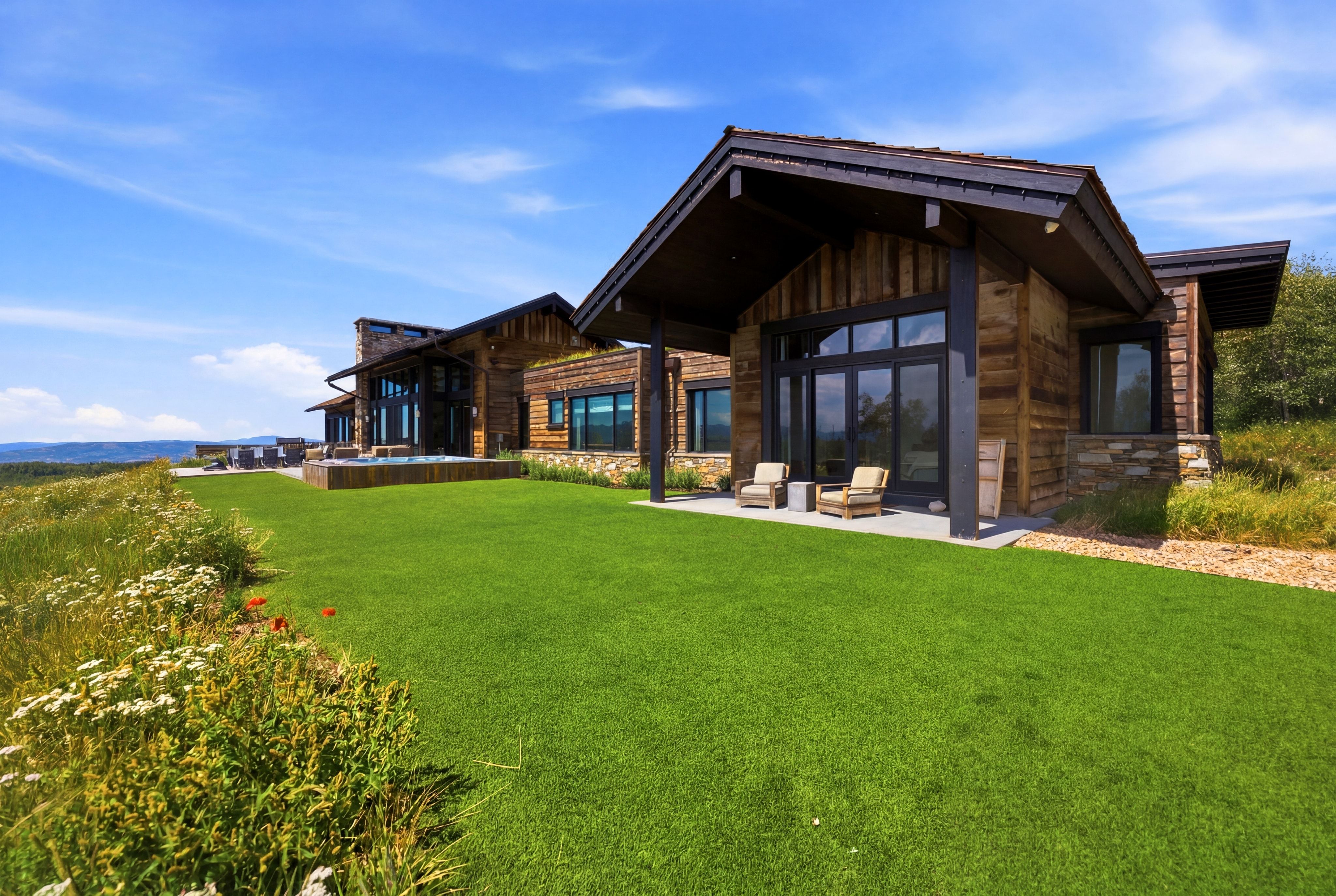 Expansive green lawn with a custom-built home featuring wood siding, stone accents, and large glass doors
