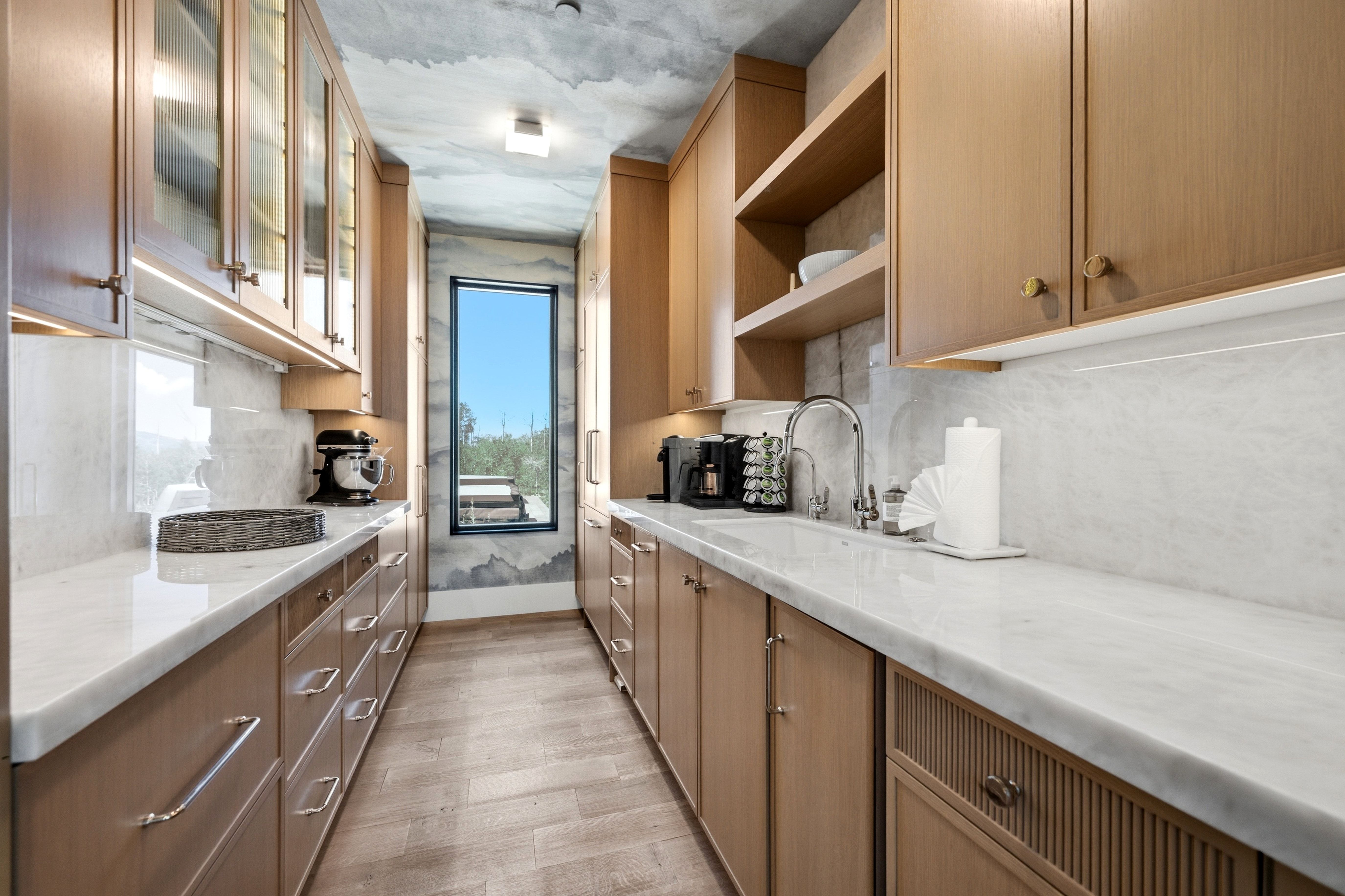 Galley kitchen featuring light wood cabinetry, white countertops, and a white tile backsplash