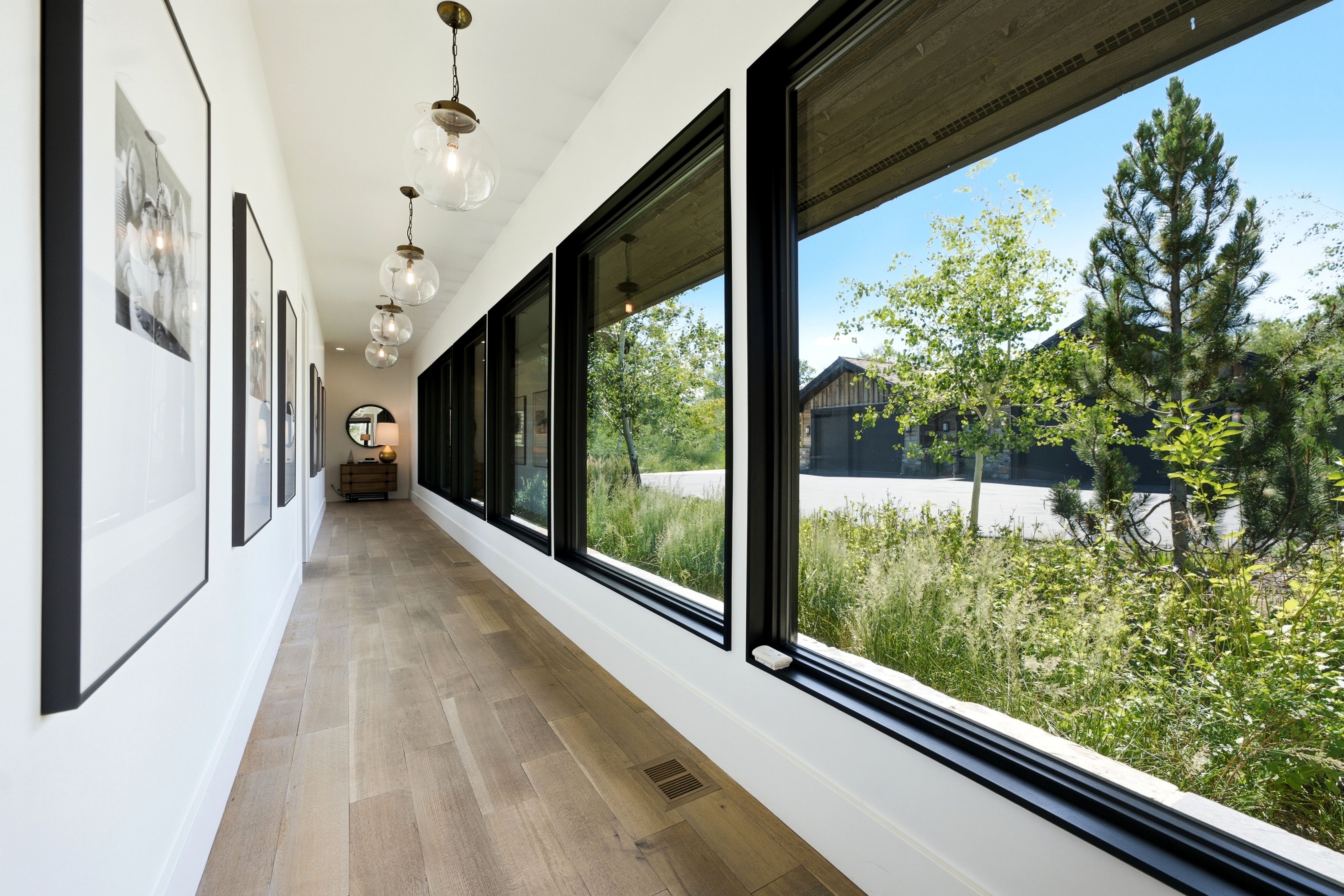 Hallway with wood-finish flooring, a wall of black-framed windows, and globe pendant lighting fixtures