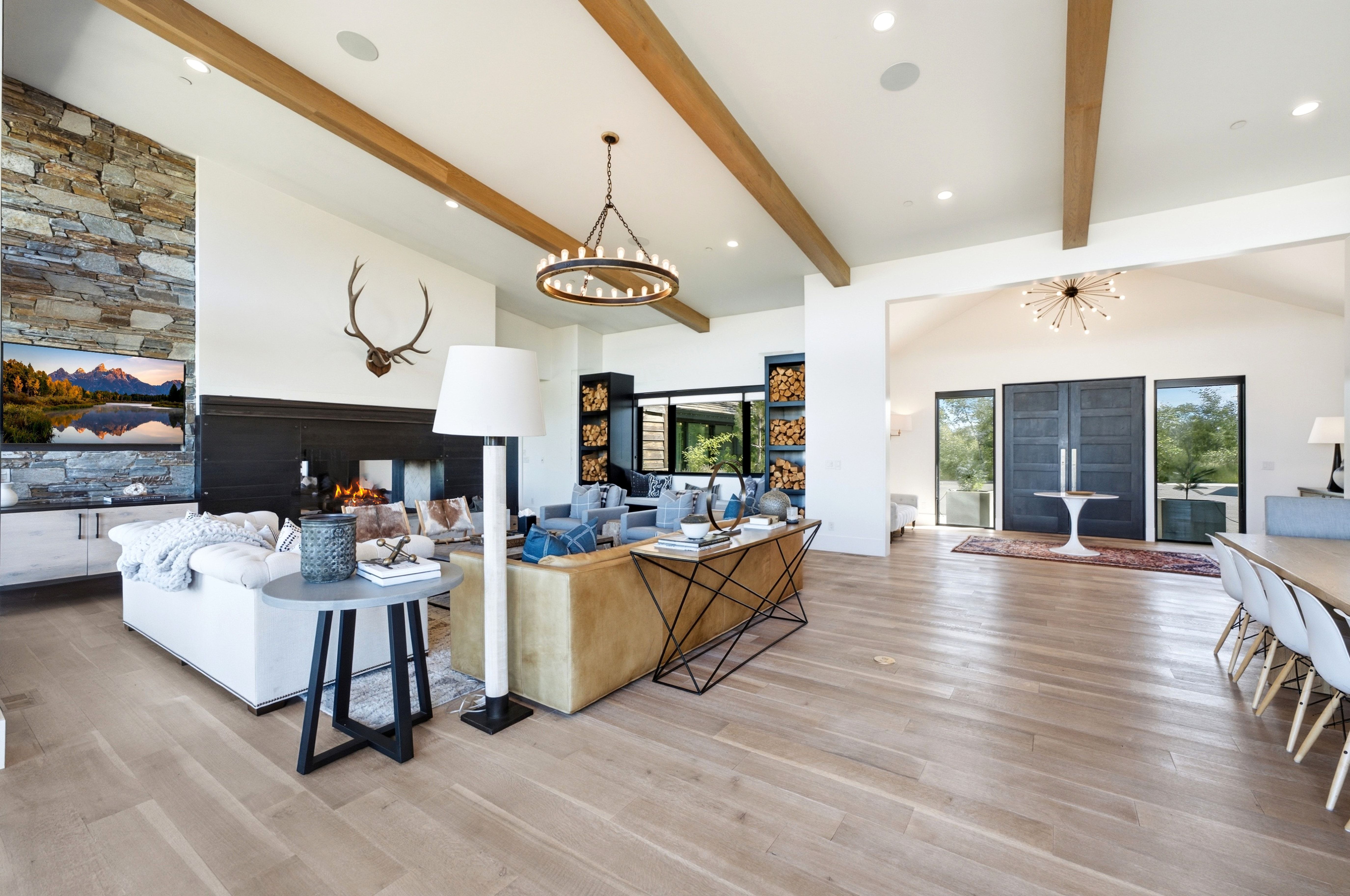Spacious living area featuring light wood-finish flooring, exposed ceiling beams, and a stone accent wall with built-in fireplace