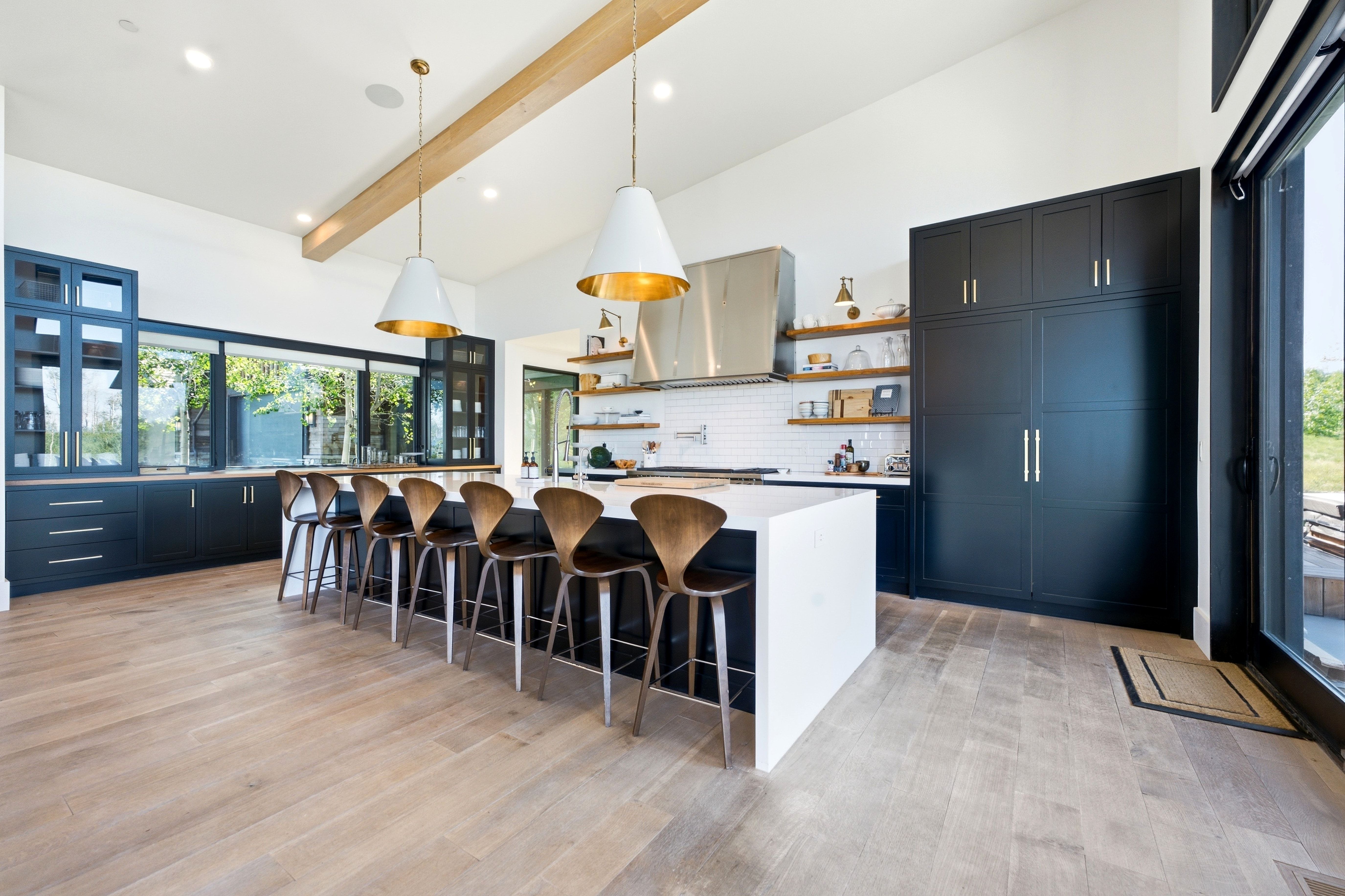 Spacious kitchen featuring an oversized island with seating, extensive dark cabinetry, wood-finish flooring, a white subway tile backsplash, and stainless steel appliances