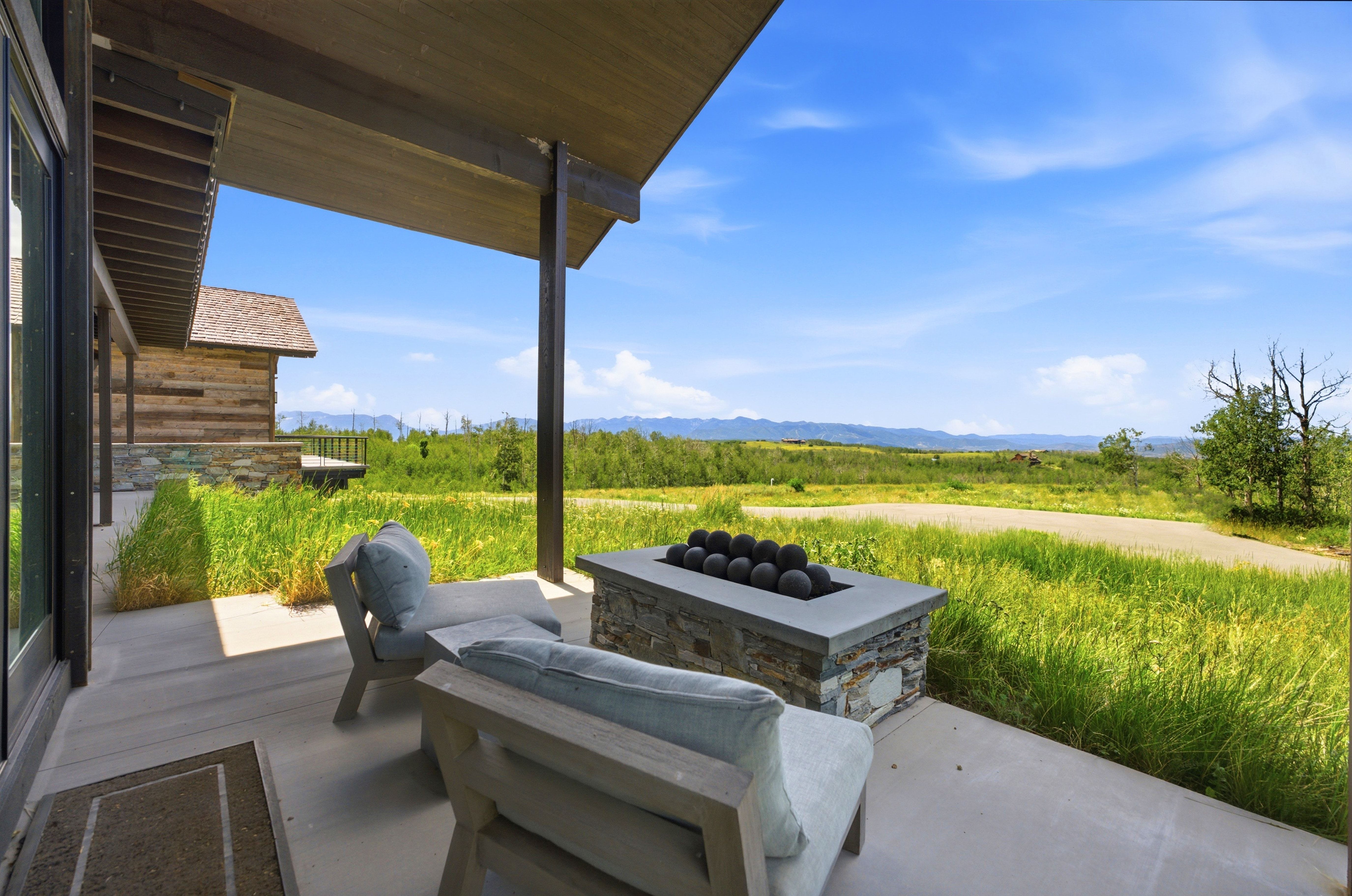 Spacious outdoor patio featuring a stone-clad fire pit, concrete surface, and wood-beam overhang