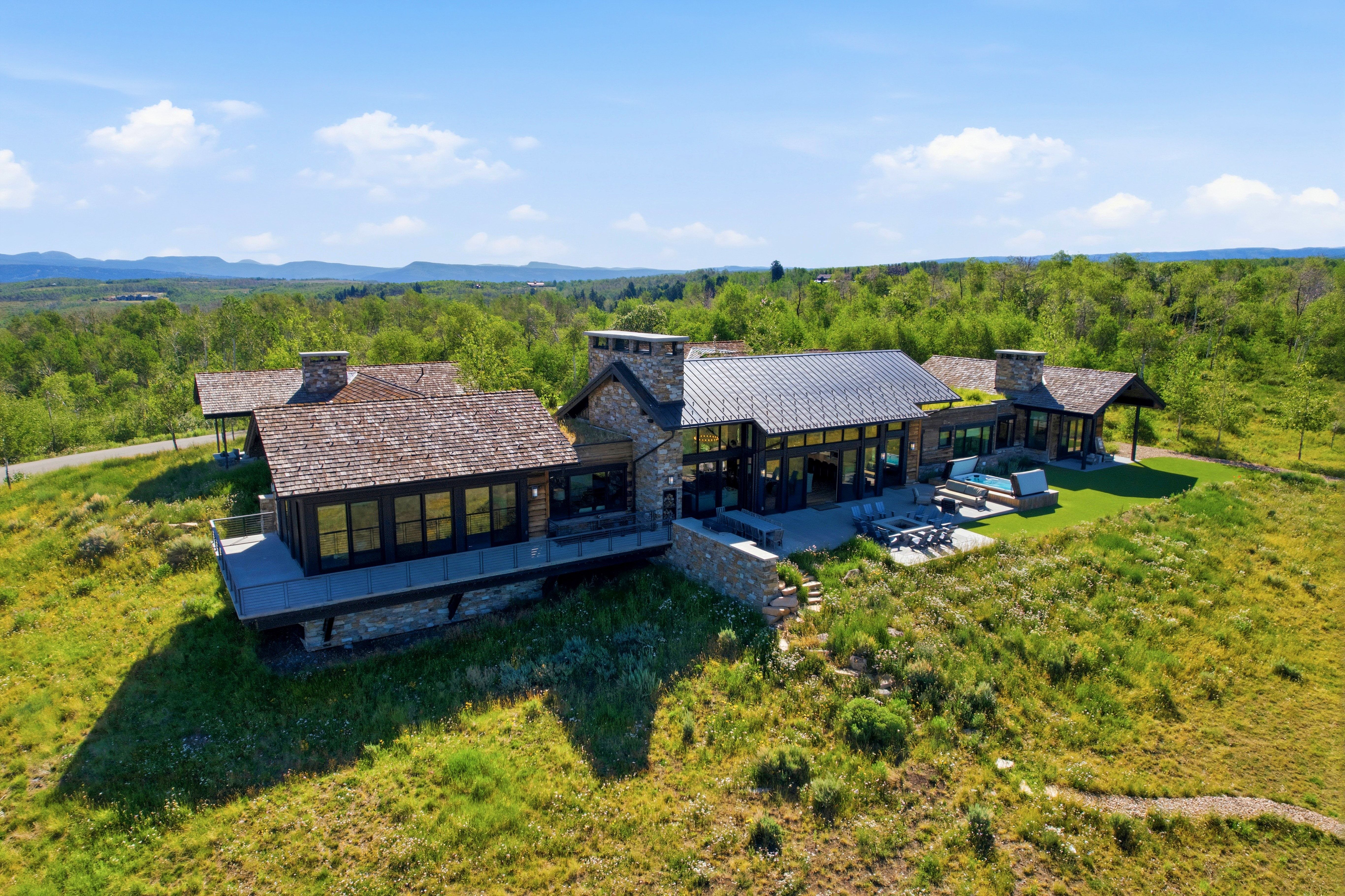 Expansive property featuring a stone and wood exterior, multiple outdoor patio areas, a flat lawn, and a natural, verdant landscape