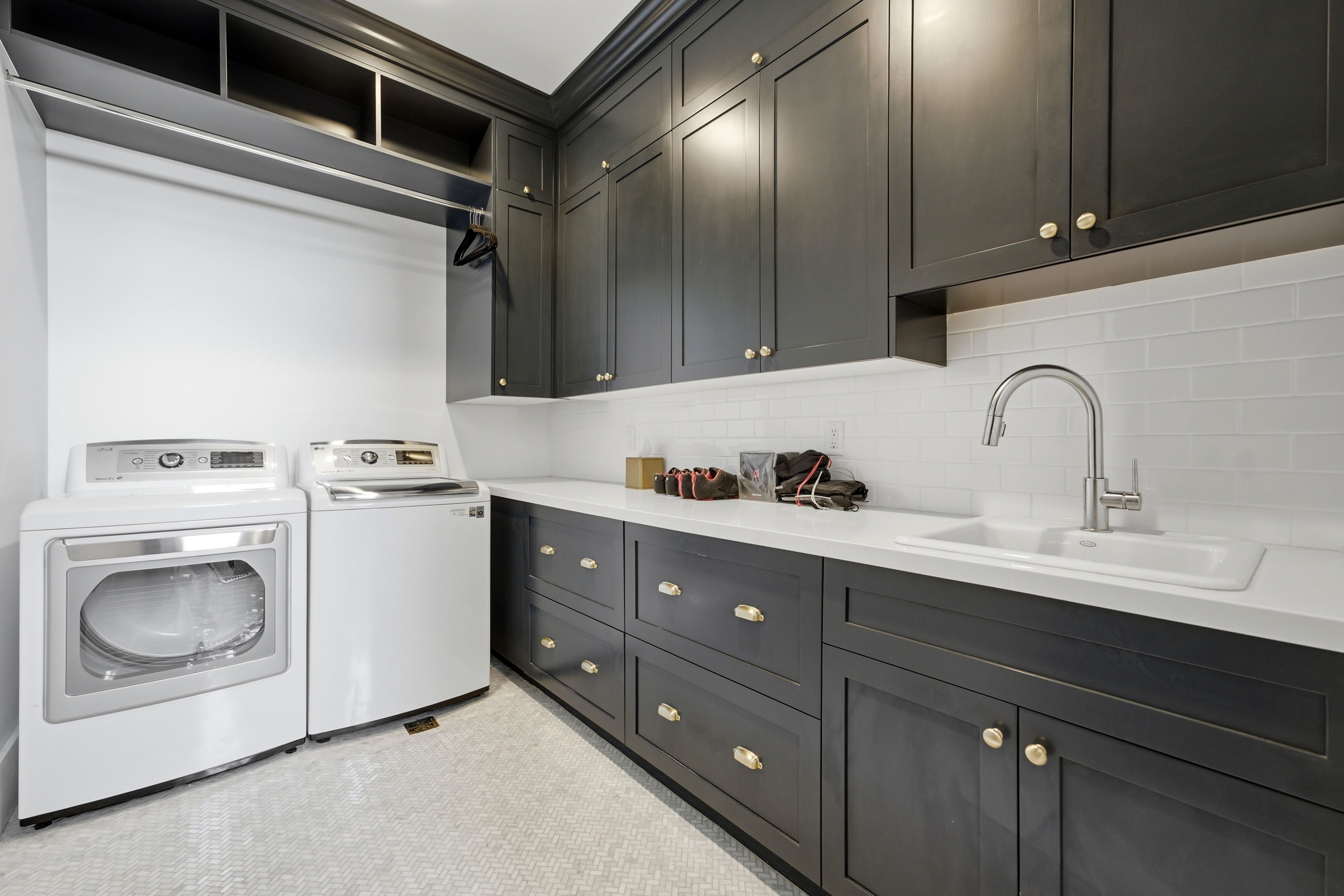 Laundry room featuring extensive dark cabinetry with gold-toned hardware, white countertops, and a white subway tile backsplash