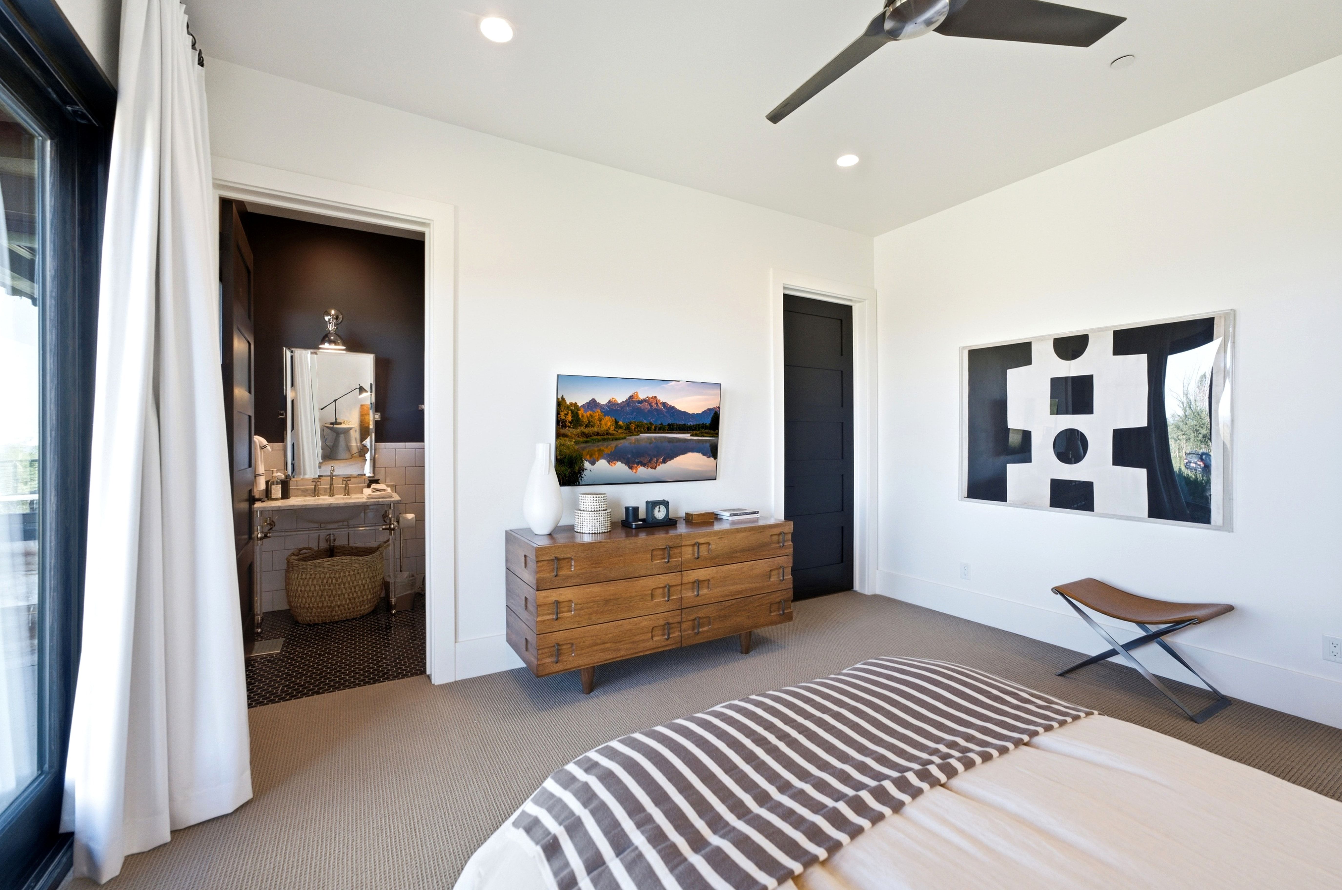 Spacious room featuring neutral carpeting, a dark ceiling fan, recessed lighting, and a doorway opening to a bathroom with a vanity and patterned floor