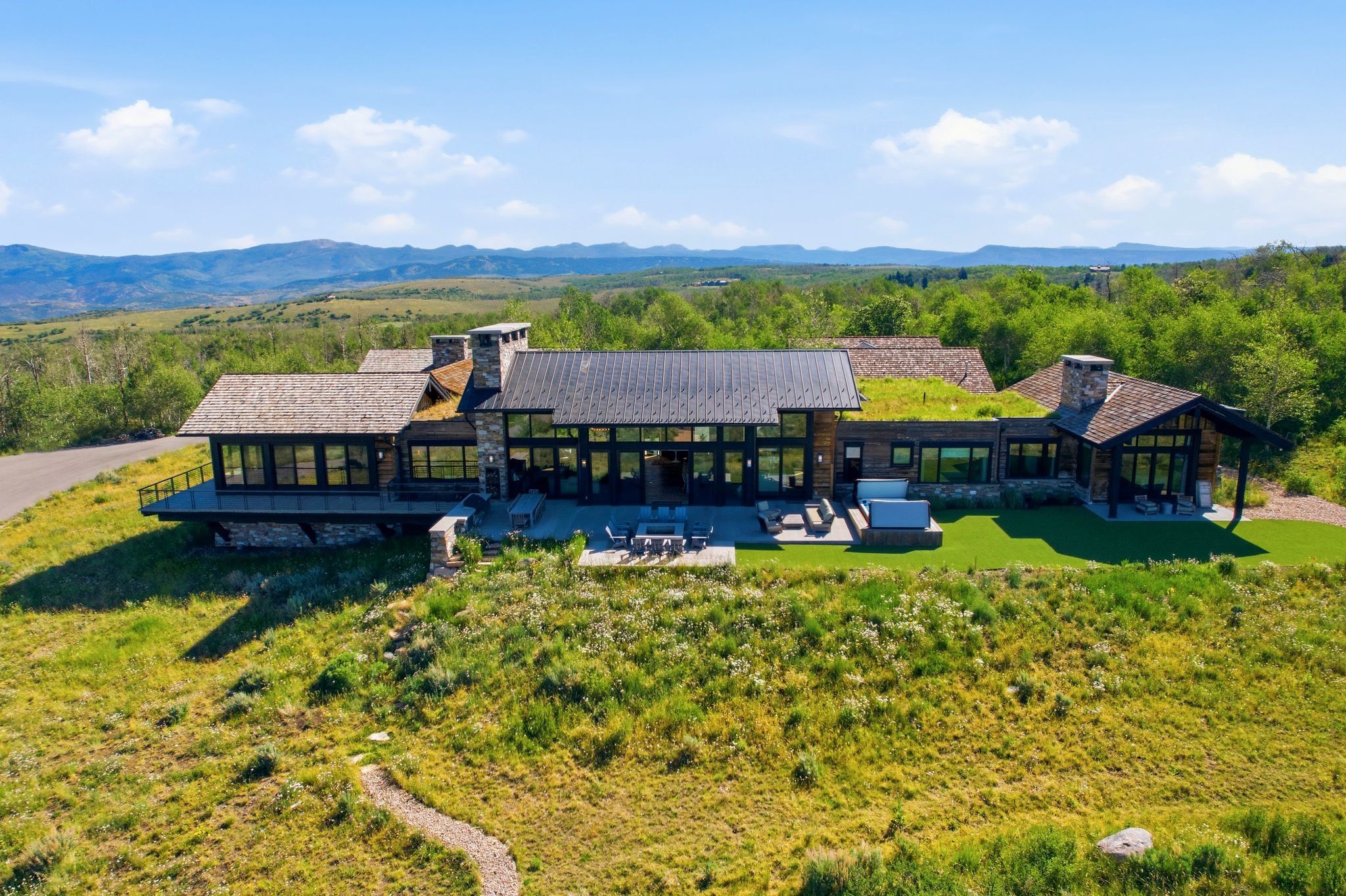 Contemporary architectural design featuring extensive glass window walls, a metal roof, and a prominent stone chimney