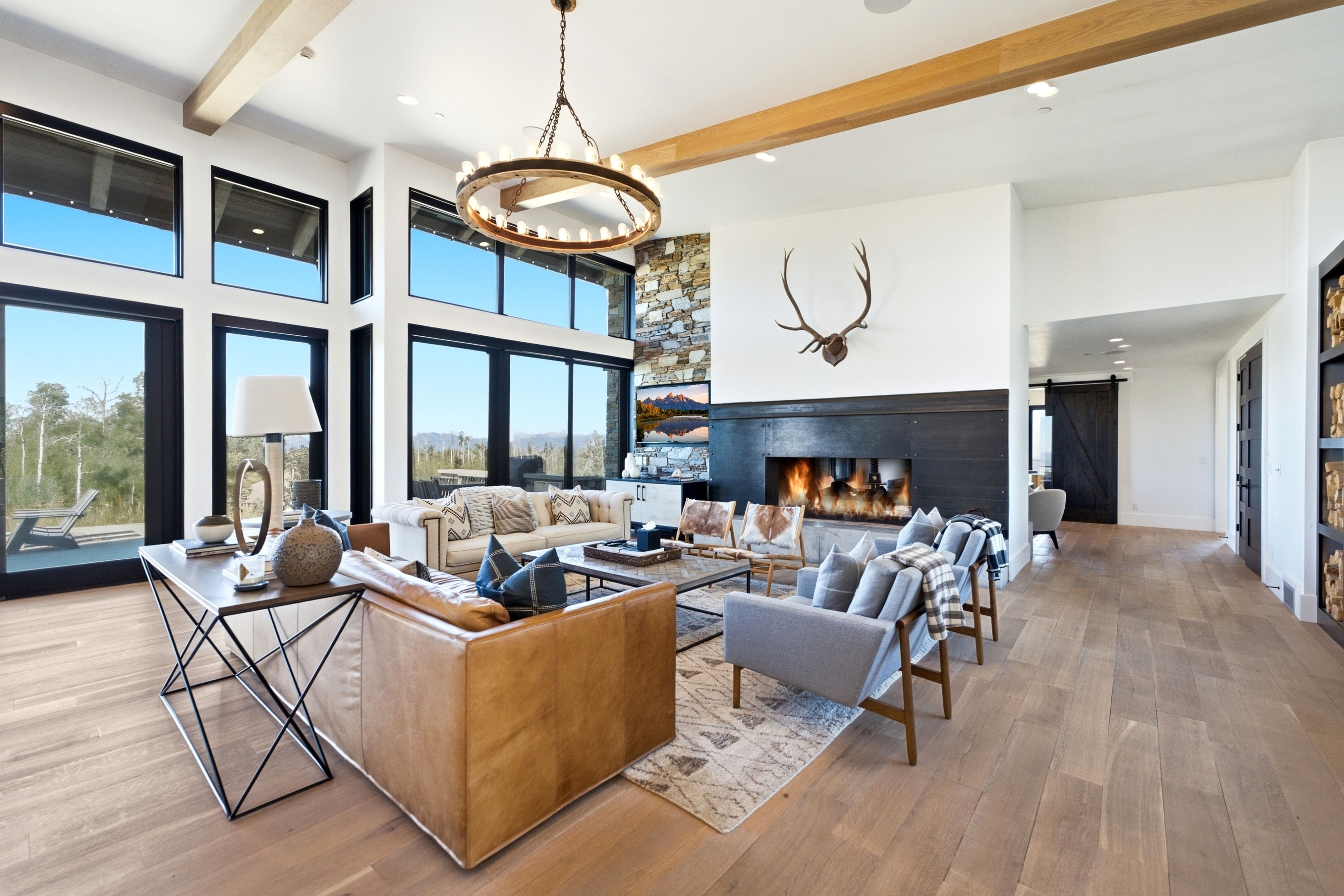 Great room featuring a full-height stone accent wall, a linear gas fireplace with a dark wood mantel, and expansive floor-to-ceiling windows