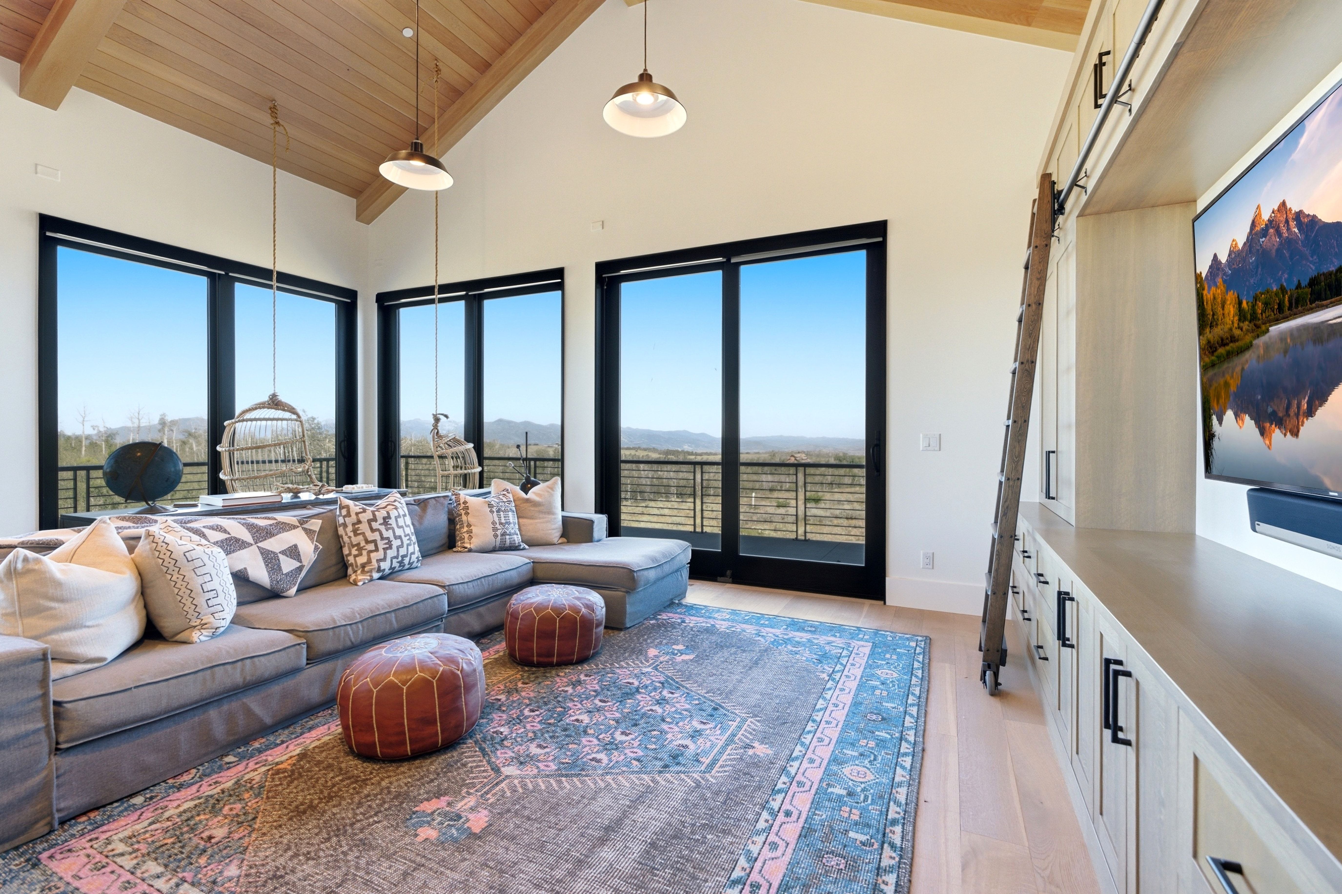 Vaulted ceiling with wood-finish planks, large black-framed windows, built-in entertainment center with storage, light wood-finish flooring, and pendant lighting fixtures