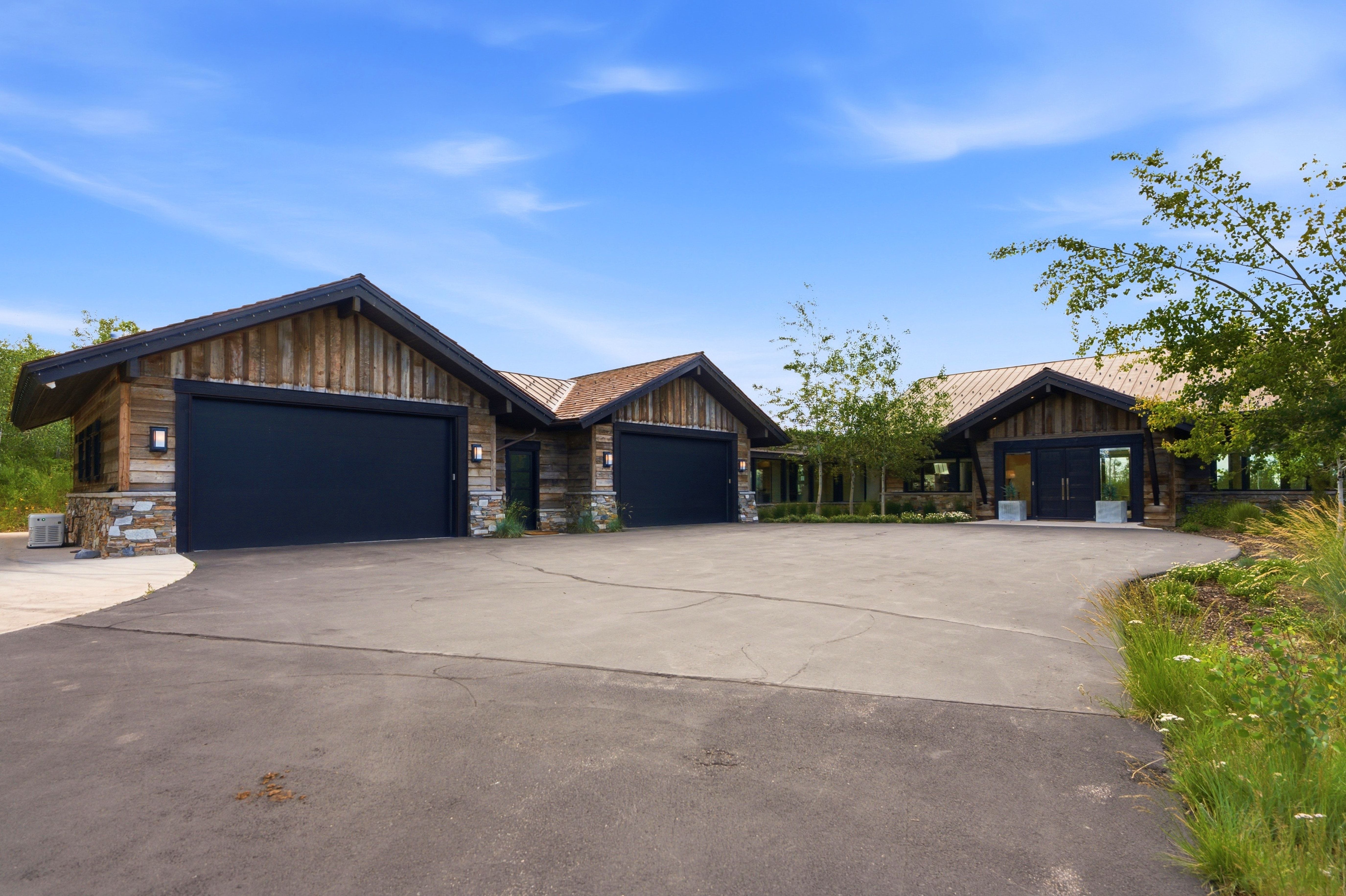 Expansive paved driveway leading to a multi-car garage with black doors